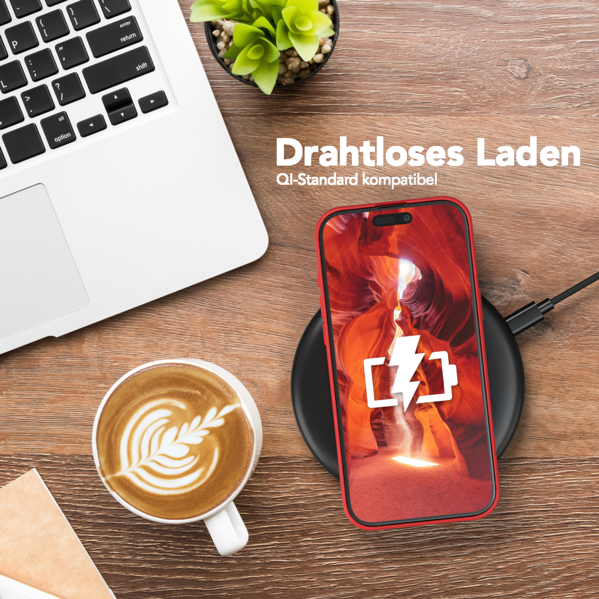 Laptop, Telefon laden, Kaffee und eine Pflanze auf einem Holzschreibtisch. Das Telefon zeigt ein Ladesymbol.
