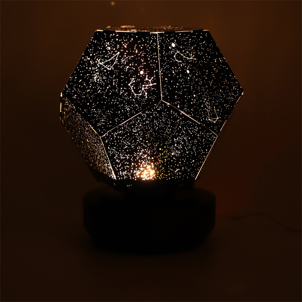 Eine Sternenprojektorlampe, mit schwarzem Sockel, projiziert Sterne auf eine dunkle Oberfläche.