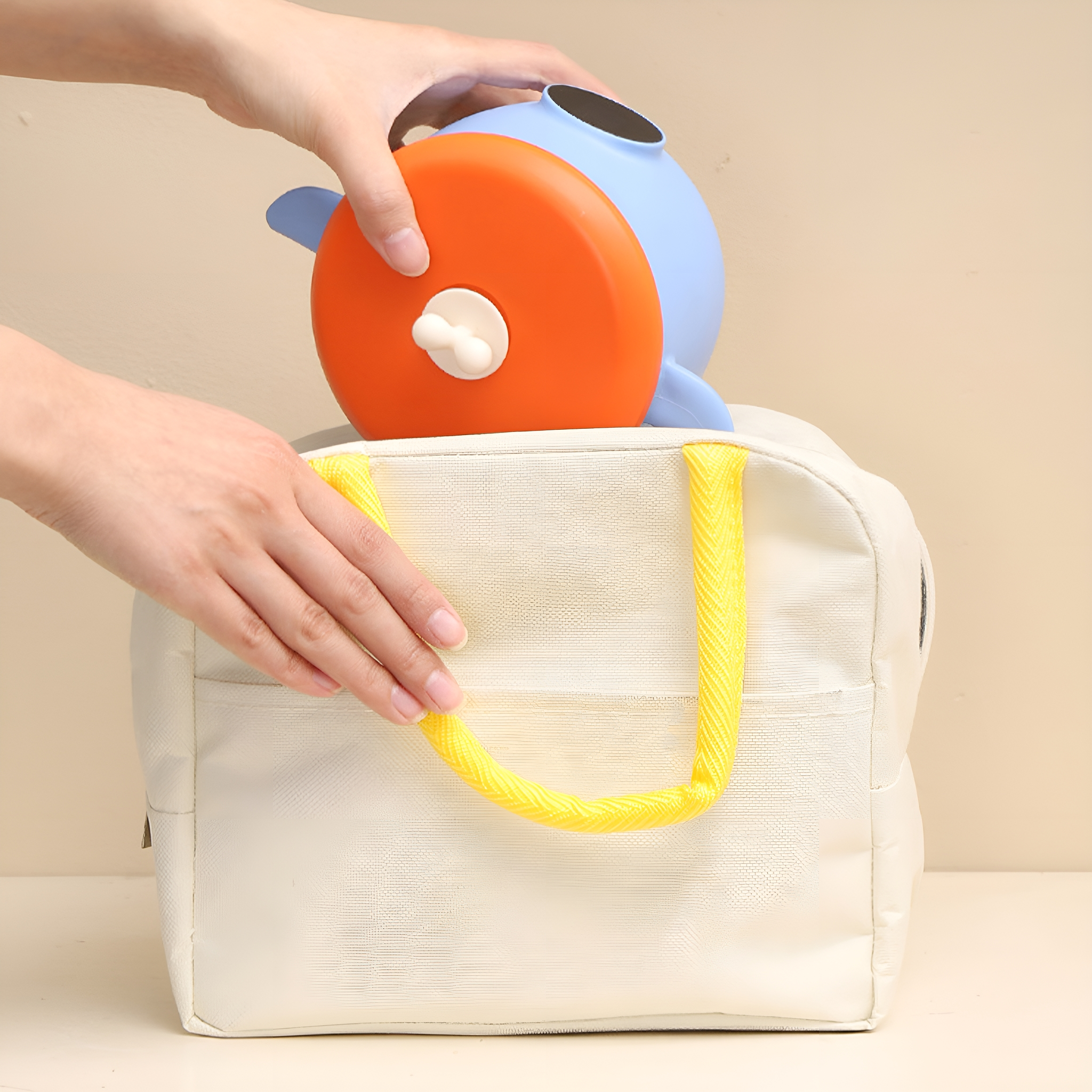 Eine Person legt ein blaues und orangefarbenes Spielzeug in eine weiße Lunchtasche mit gelbem Griff.