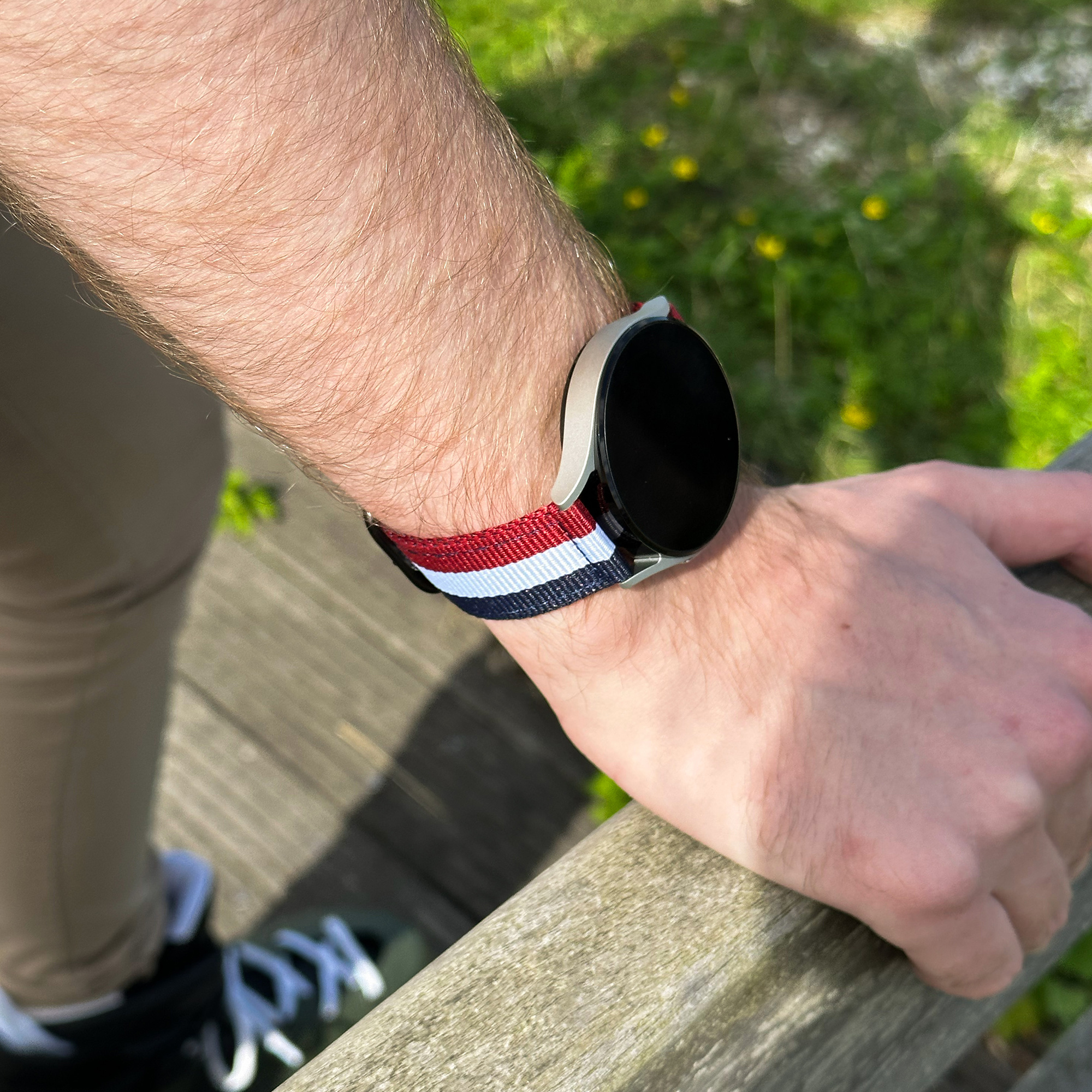 Der Arm einer Person mit einer Smartwatch und einem gestreiften Armband. Die Uhr ist schwarz und hat einen schwarzen Bildschirm.