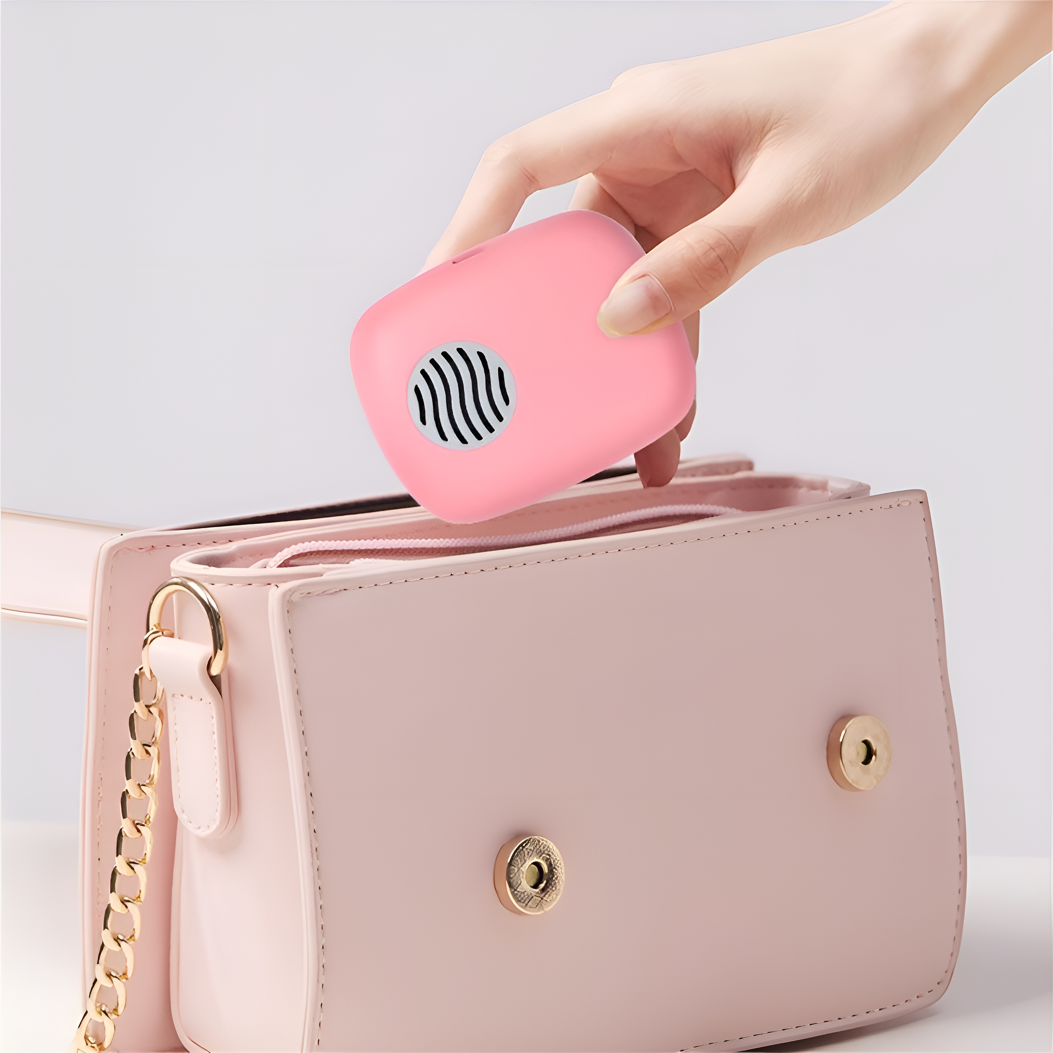 Eine Hand legt ein pinkfarbenes, quadratisches Gerät in eine pinkfarbene Handtasche.
