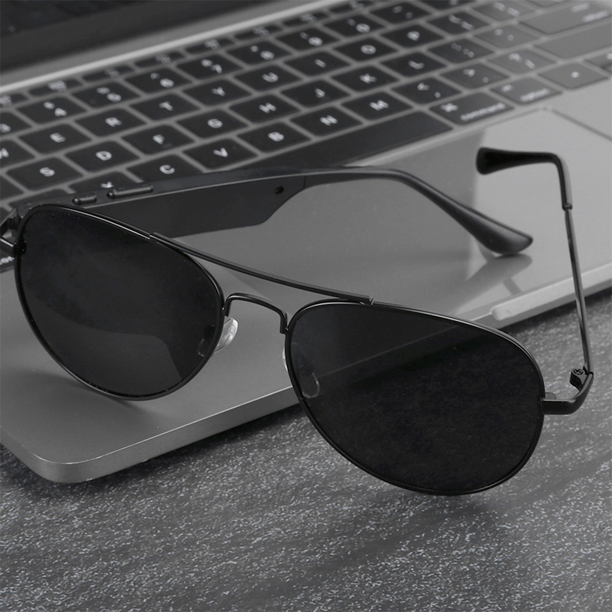 Schwarze Sonnenbrille liegt auf einer Laptop-Tastatur. Die Gläser sind dunkel. Die Szene ist drinnen auf einem Schreibtisch.