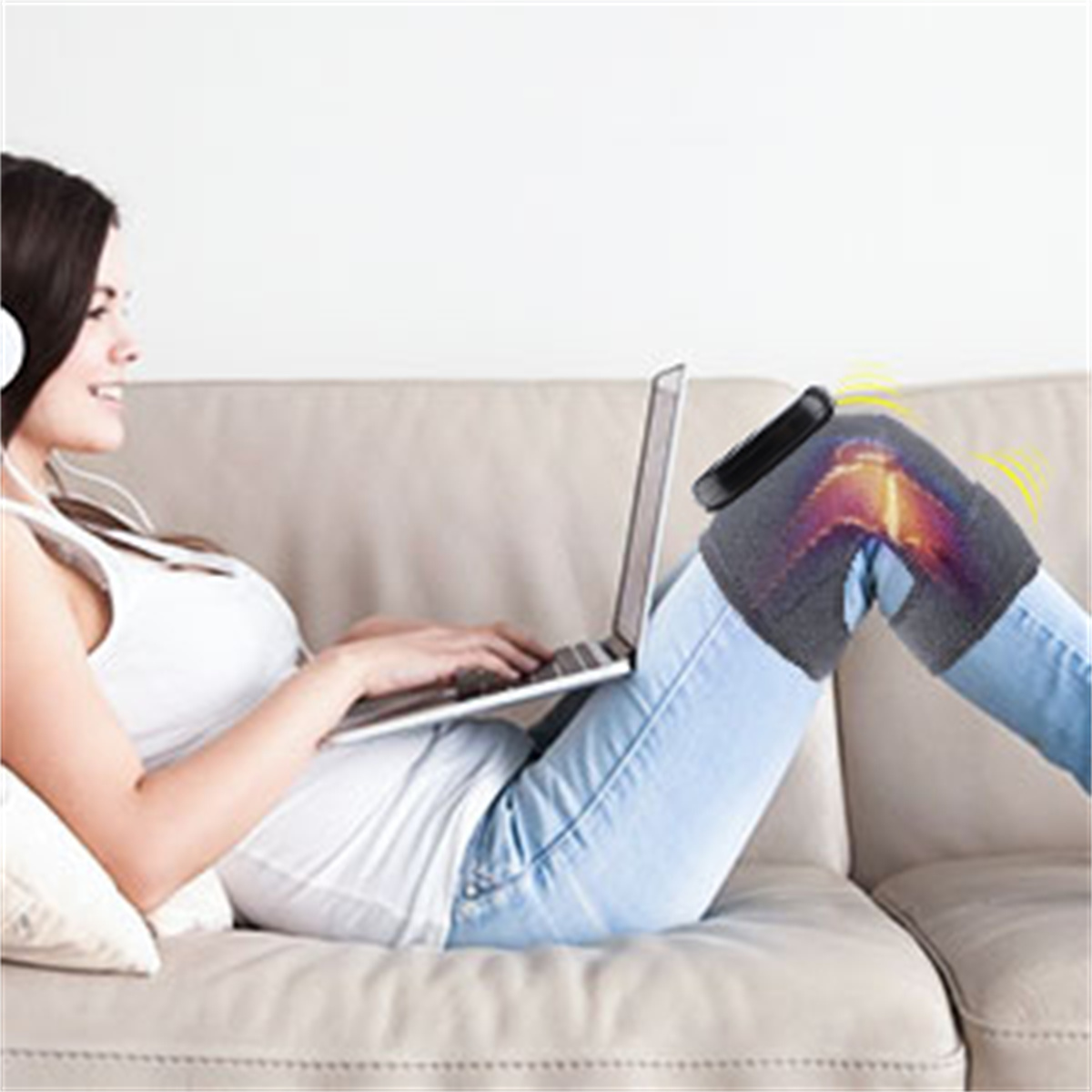 Frau auf dem Sofa mit Laptop und Kopfhörern. Kniebandage mit Wärmewellen.