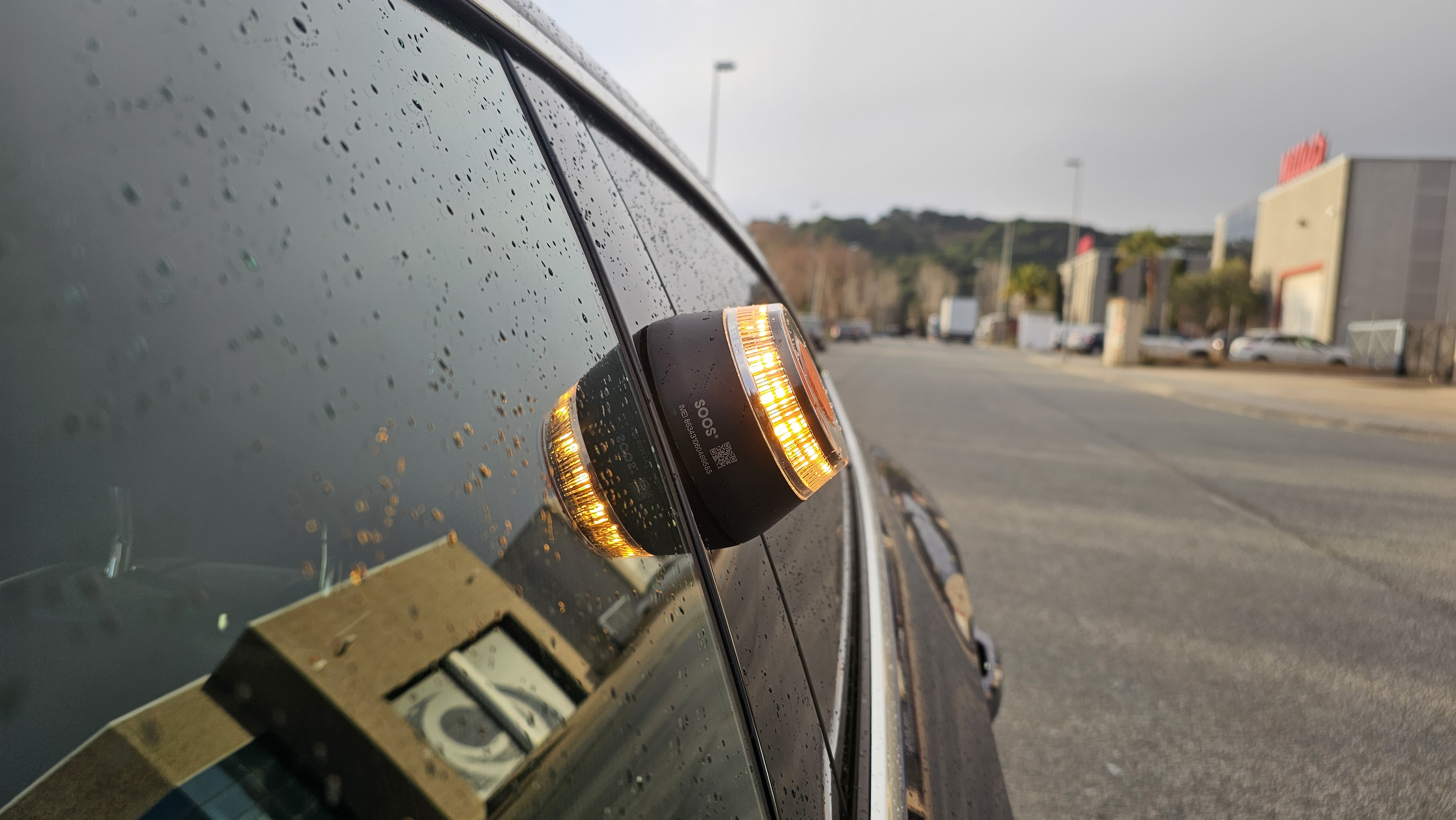 Lateral de coche con luz ámbar intermitente. La luz está encendida, reflejada en la ventana mojada.