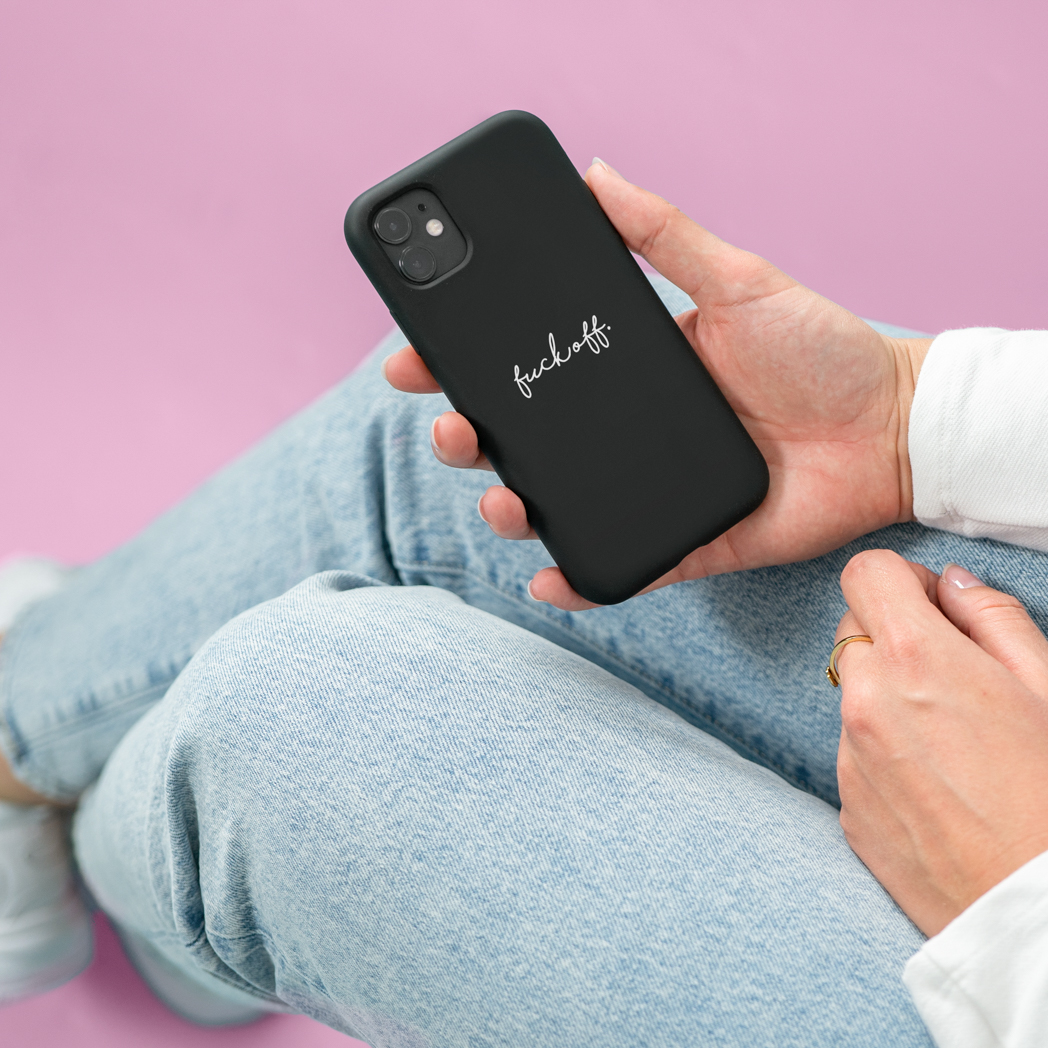 Une coque de téléphone noire avec les mots "fuck off" en écriture blanche, tenue dans la main d'une personne.