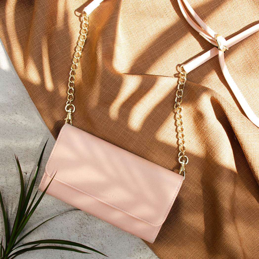 Sac à main rose avec une chaîne dorée, posé sur du tissu marron. Vue de dessus.