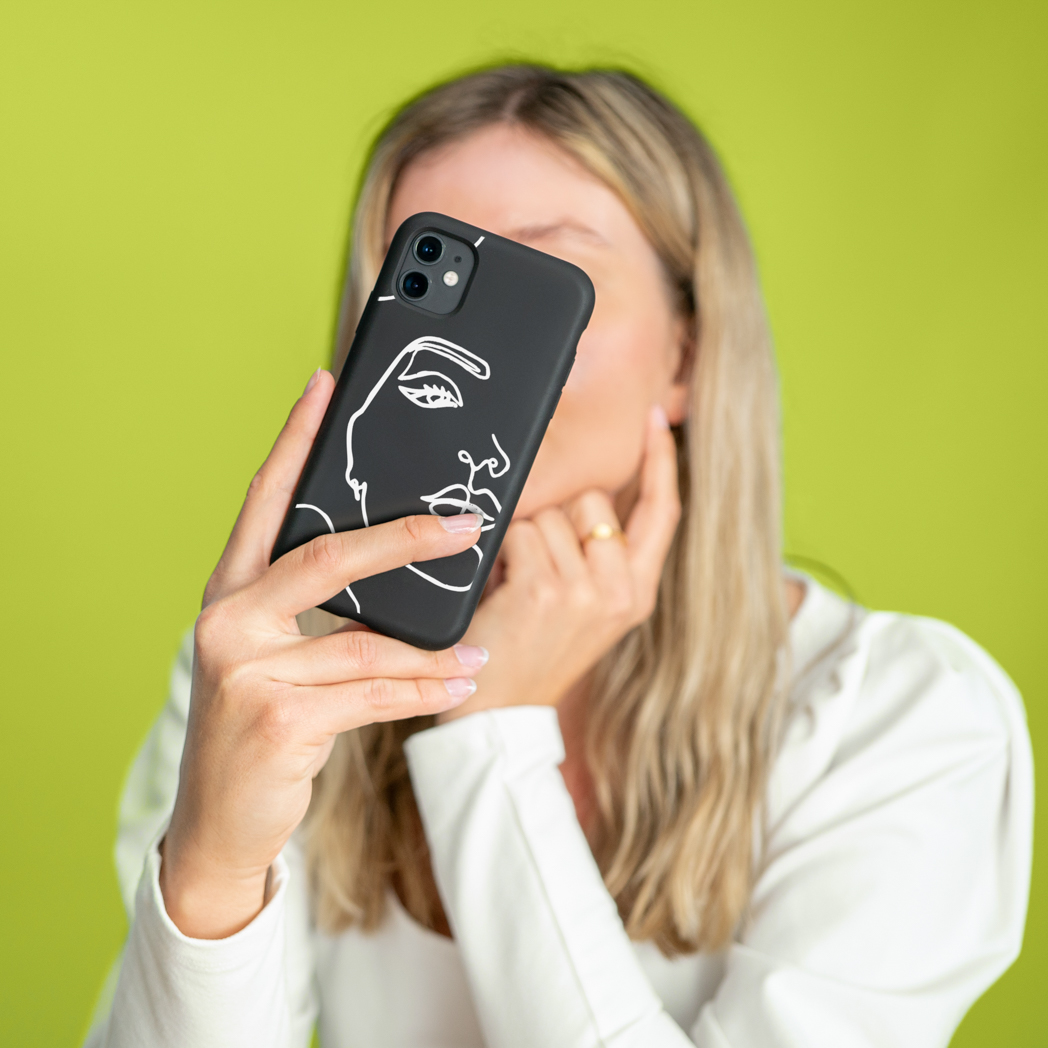 Een persoon houdt een telefoon vast. De telefoon zit in een zwarte hoes met een witte omtrek van een gezicht.