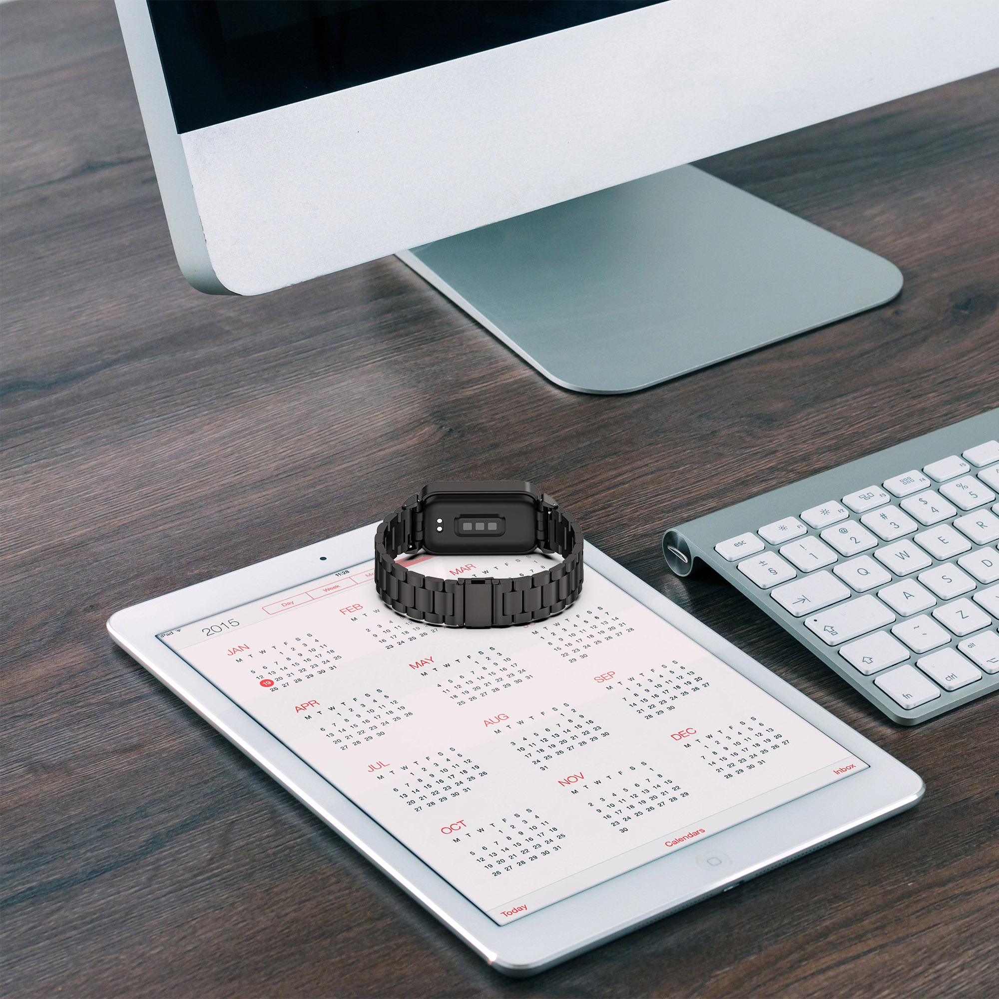 Ein schwarzes Armband mit Bildschirm auf einem Tablet und Kalender auf einem Holzschreibtisch.