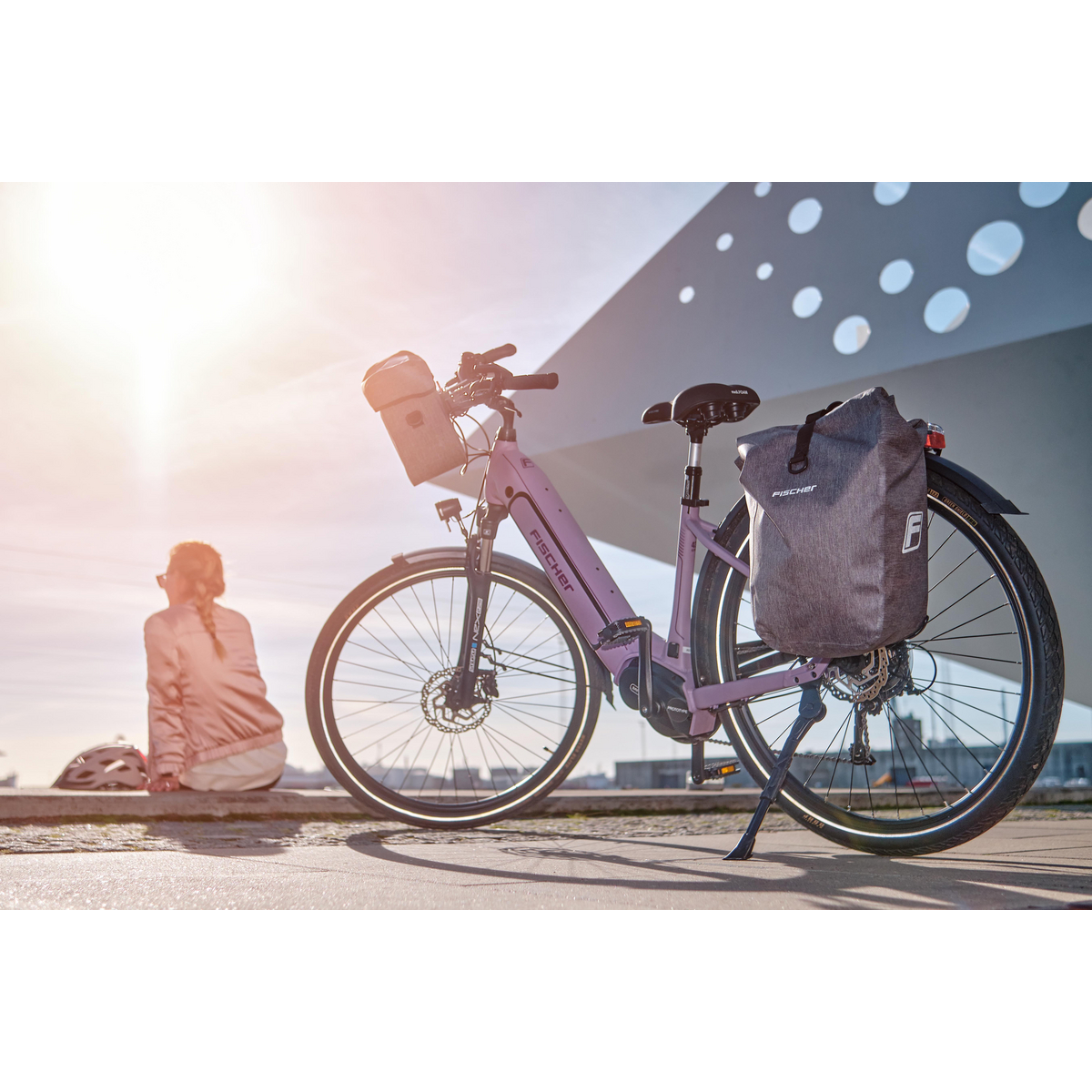 Eine Frau sitzt und betrachtet ein lila E-Bike, das auf einem Bürgersteig geparkt ist, mit einer grauen Tasche hinten.