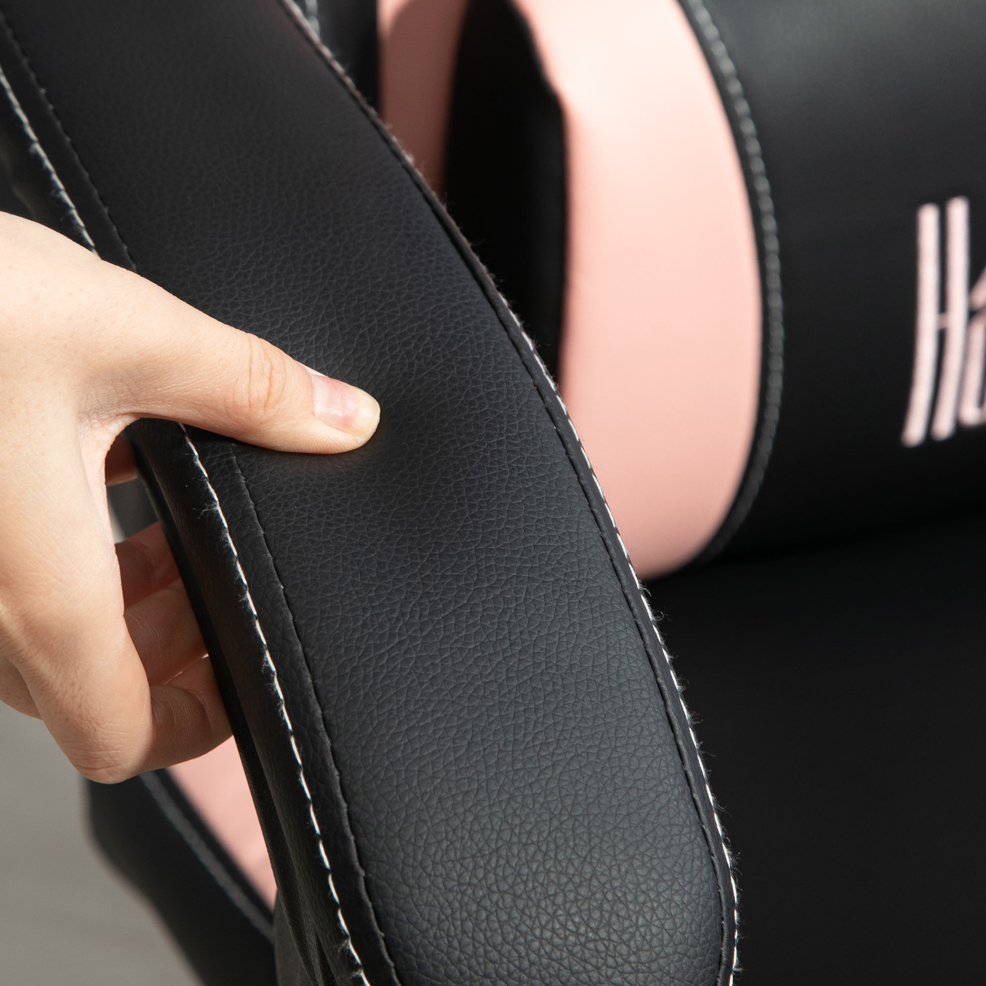 Una mano tocca il bracciolo in pelle nera di una sedia da gioco rosa e nera.