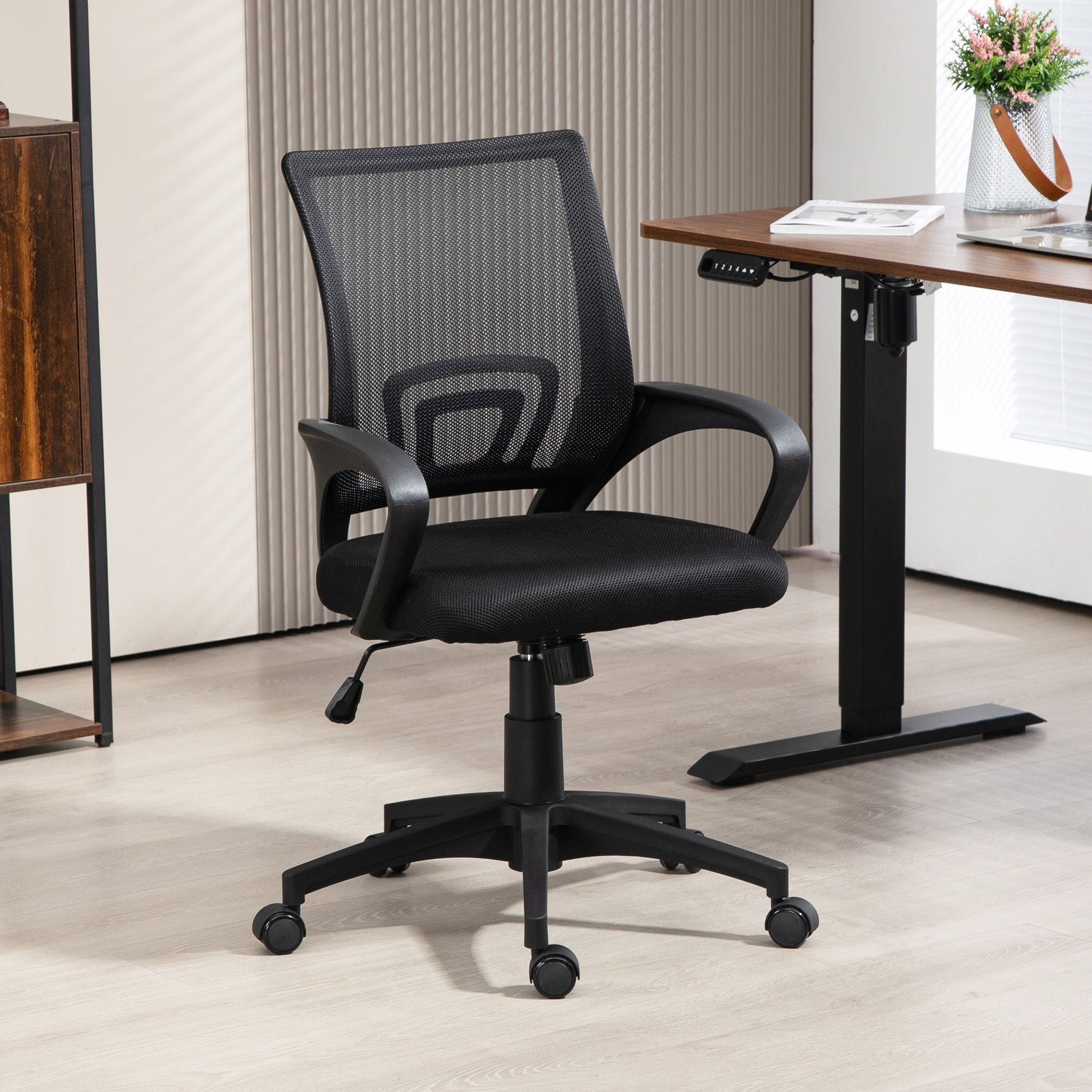 Una silla de oficina negra con respaldo de malla, ruedas y una palanca de ajuste de altura, en un entorno de oficina.