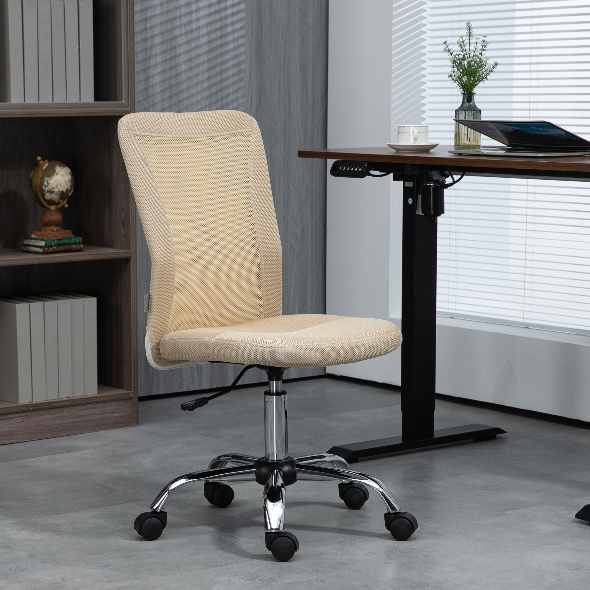 Silla de oficina de malla beige, base cromada, con escritorio, libros y ventana al fondo.