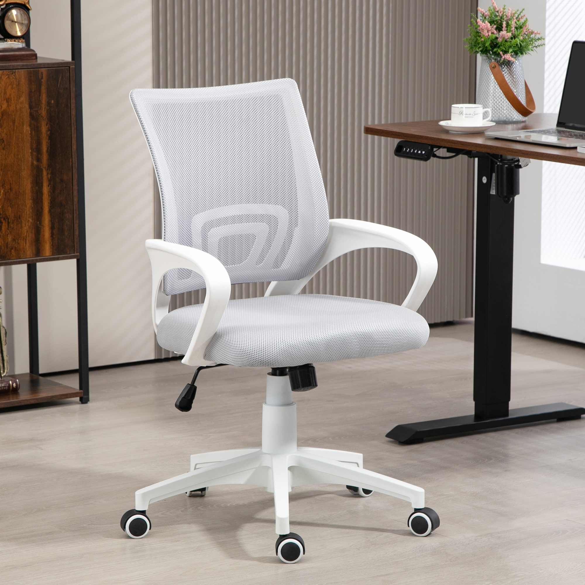 Silla de oficina blanca con respaldo de malla y reposabrazos blancos. Un escritorio oscuro al fondo.