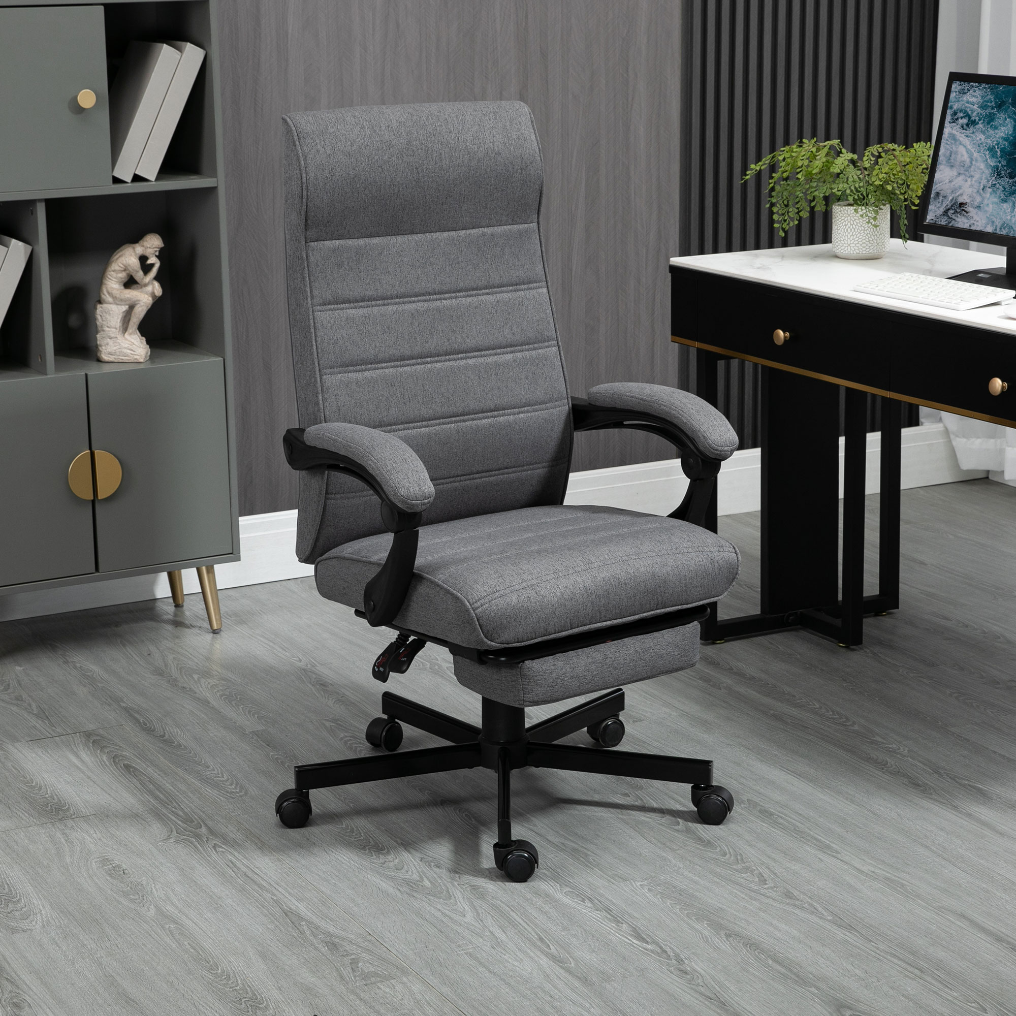 Silla de oficina gris con reposacabezas, reposabrazos y reposapiés, en un entorno de oficina en casa.