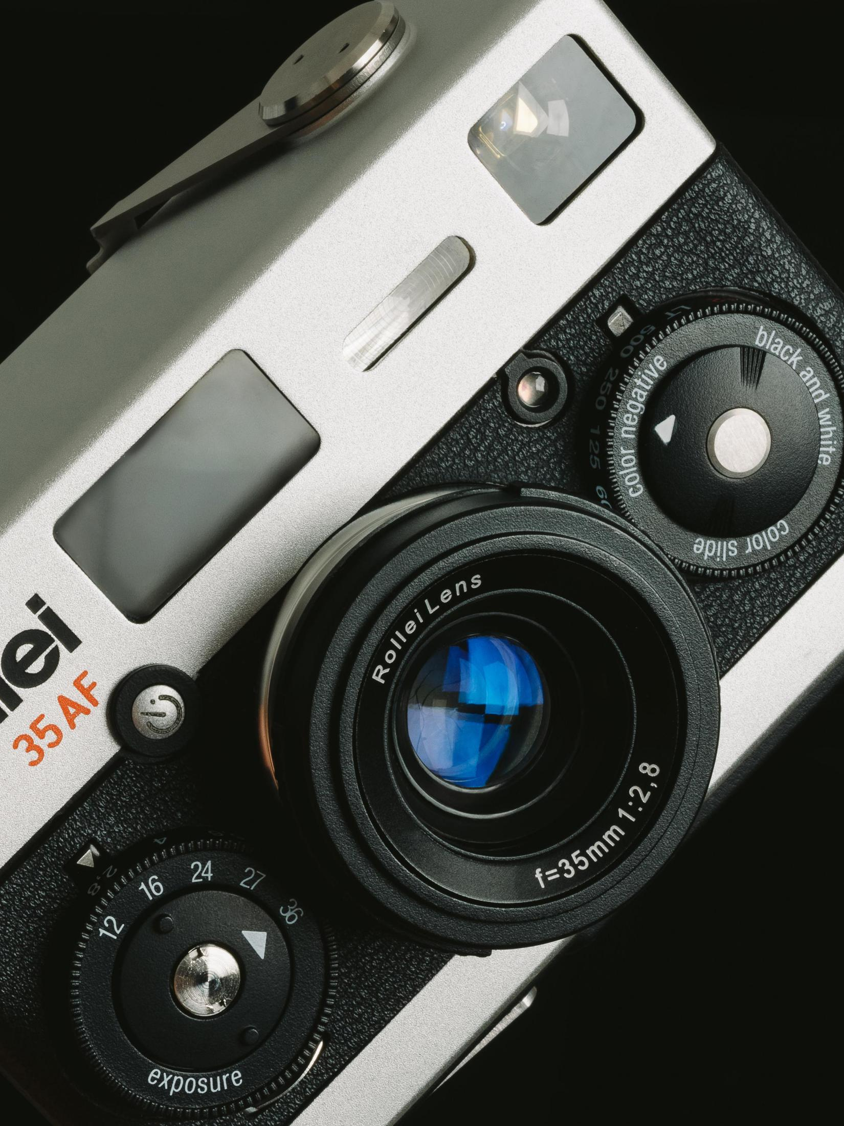 Zilver-zwarte filmcamera met lens, draaiknoppen en zoeker.