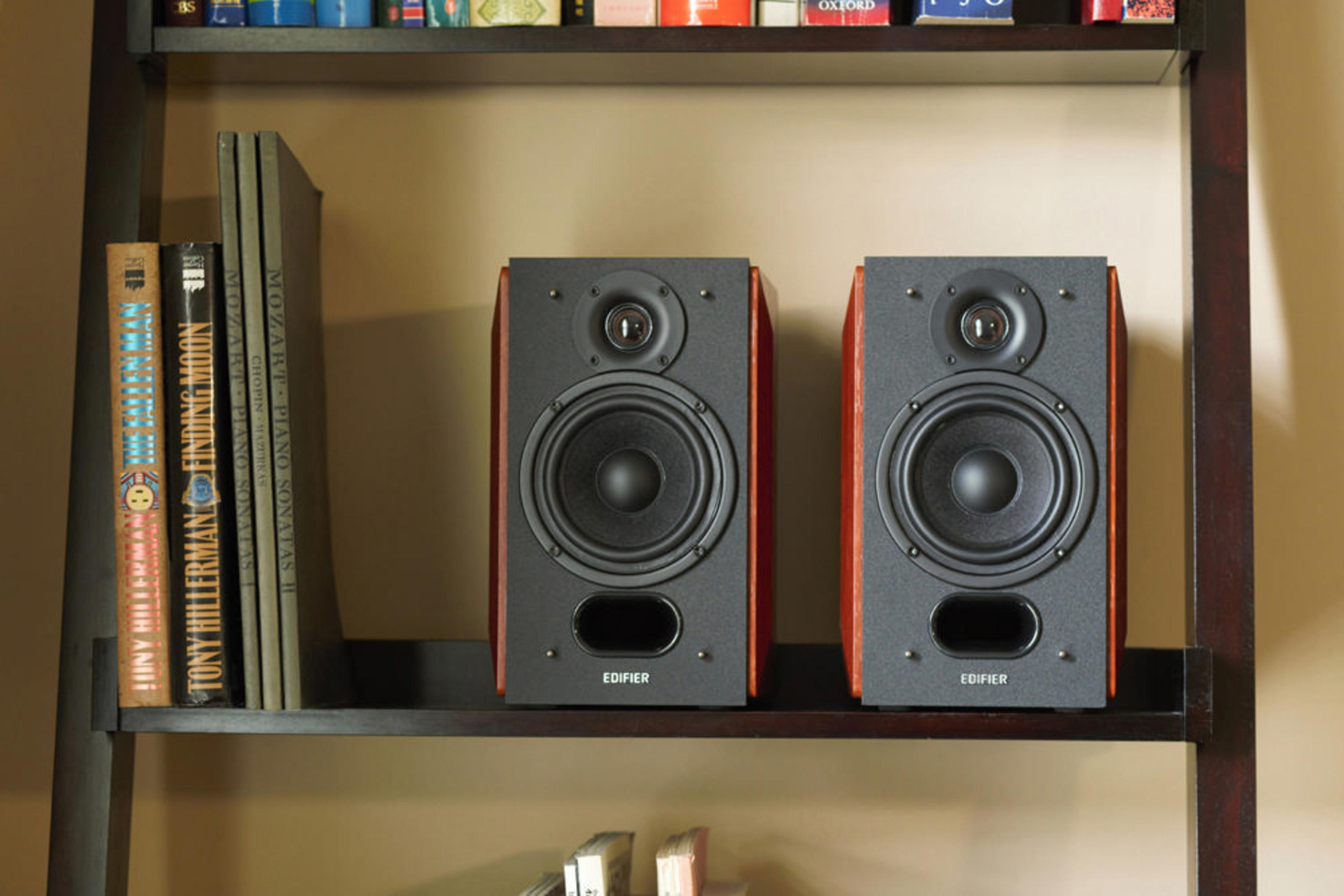 Dos altavoces negros en un estante de madera. Libros a la izquierda del estante.