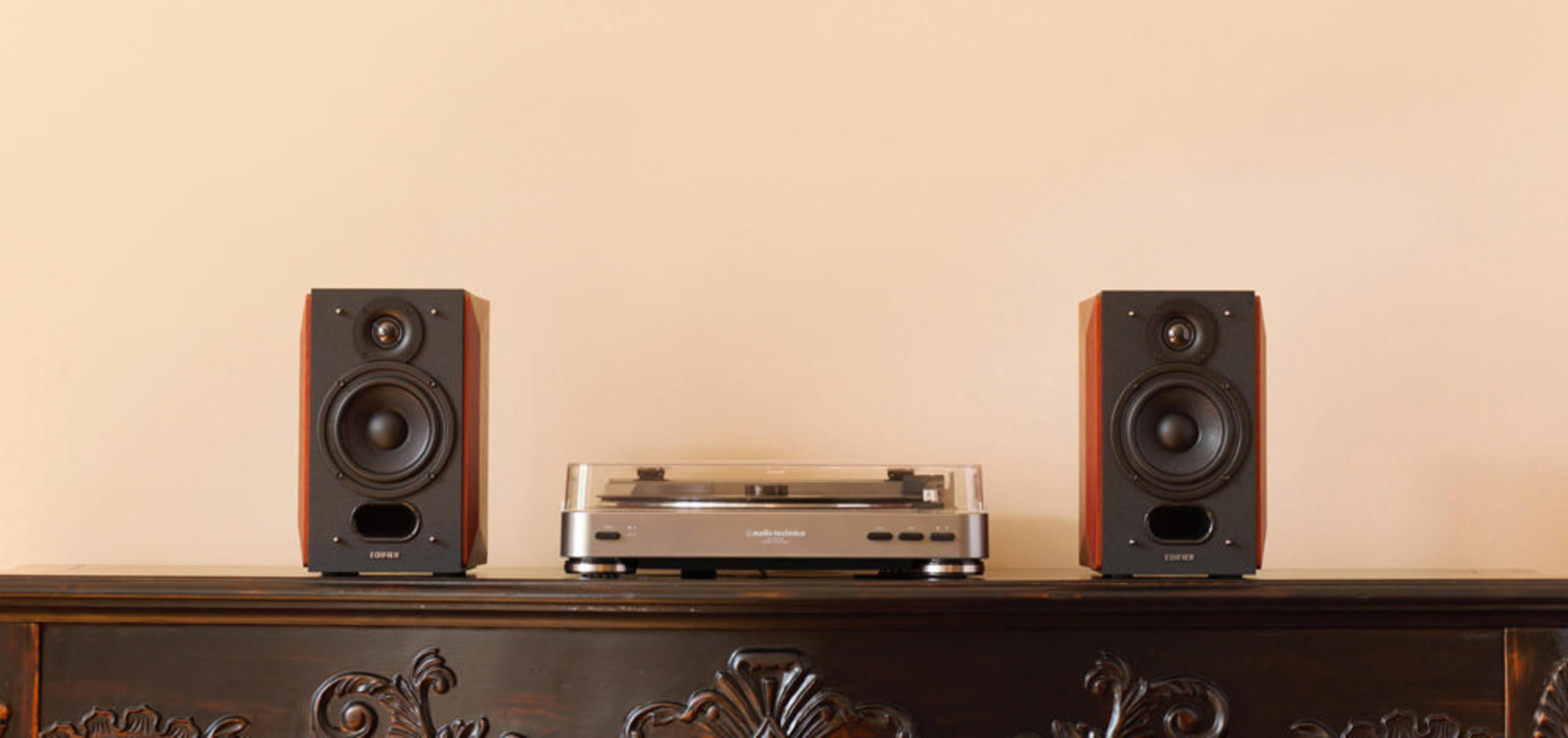Tocadiscos con dos altavoces sobre una mesa de madera oscura, pared beige.