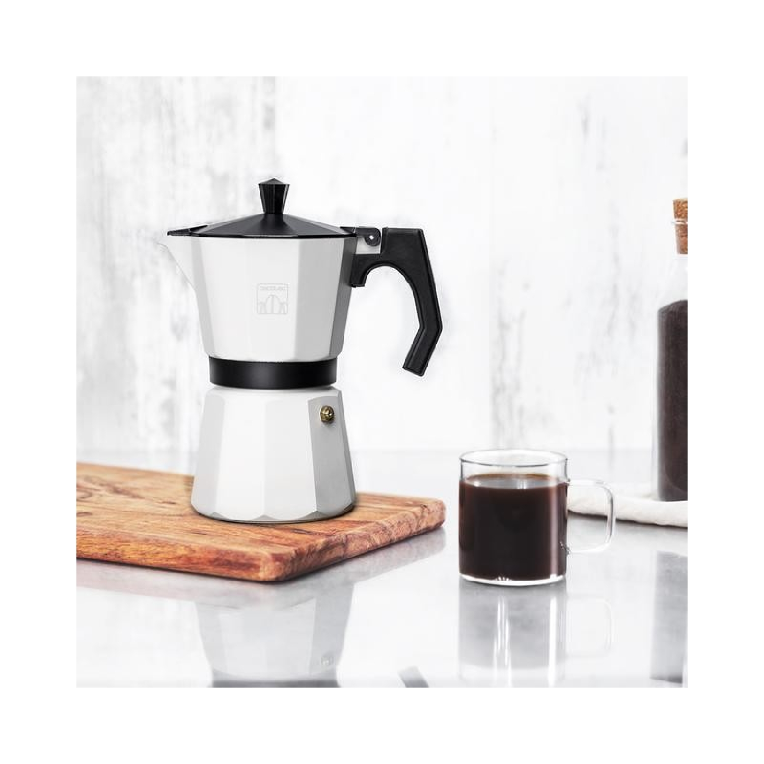 Ein weiß-schwarzer Kaffeebereiter mit einer klaren Kaffeetasse. Es steht auf einem Holzbrett.