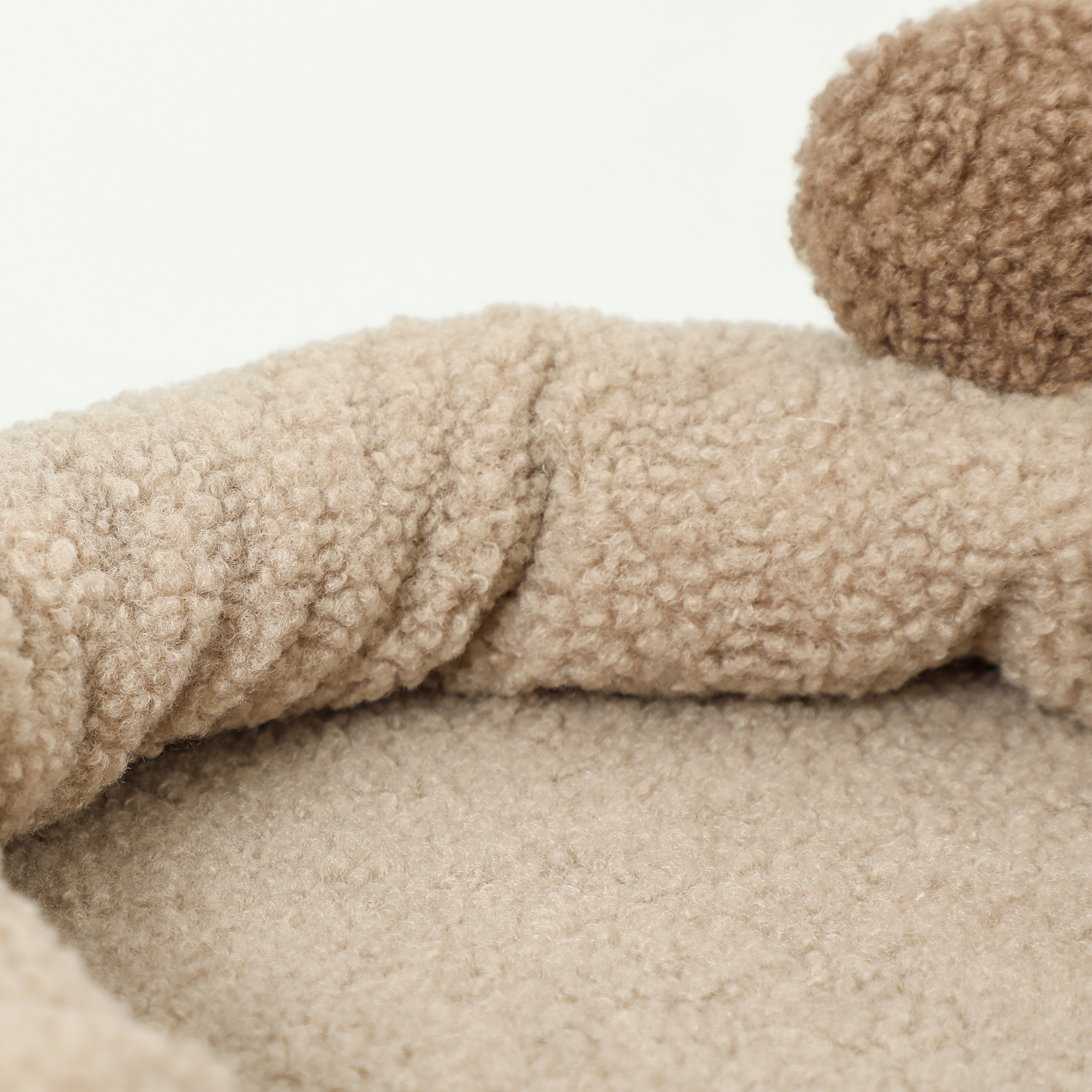 Primer plano de una cama para mascotas beige. La cama es de material suave y peludo con forma redonda.