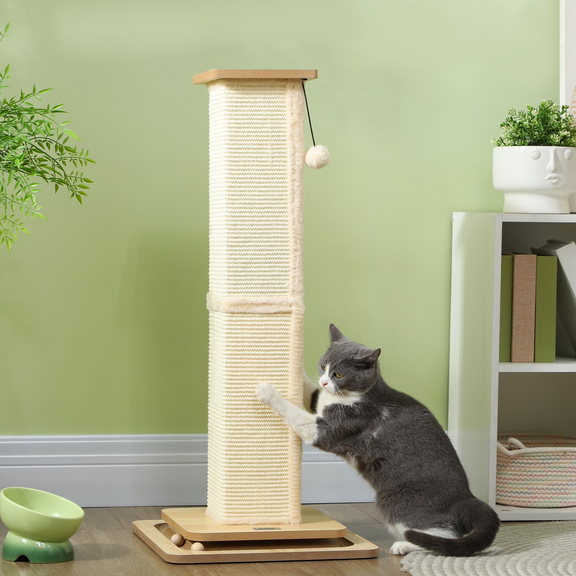 Rascador para gatos con gato juguetón, pared verde y cuenco para gatos en una habitación.