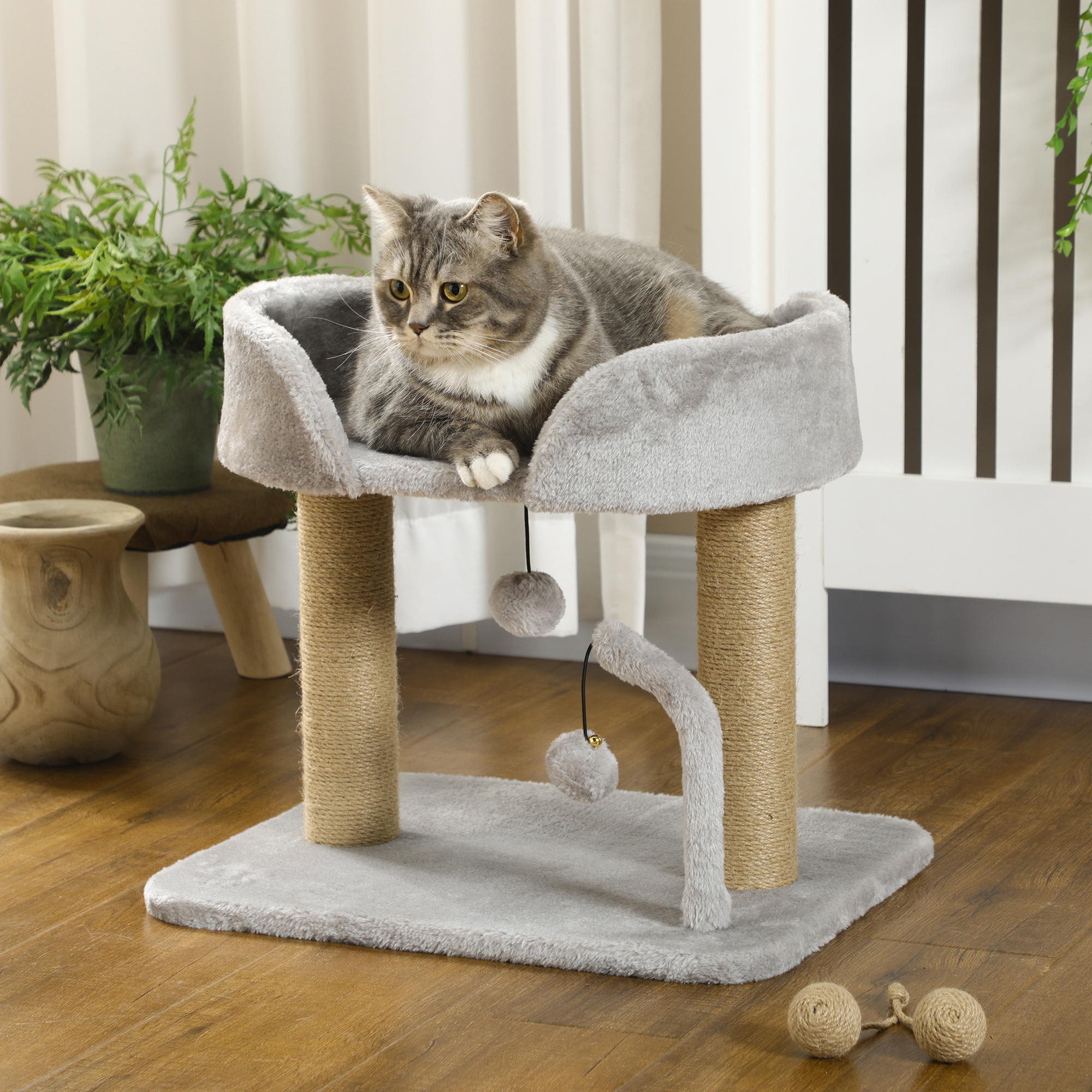 Gatto grigio su un albero per gatti grigio con un giocattolo pendente e due palline sul pavimento.