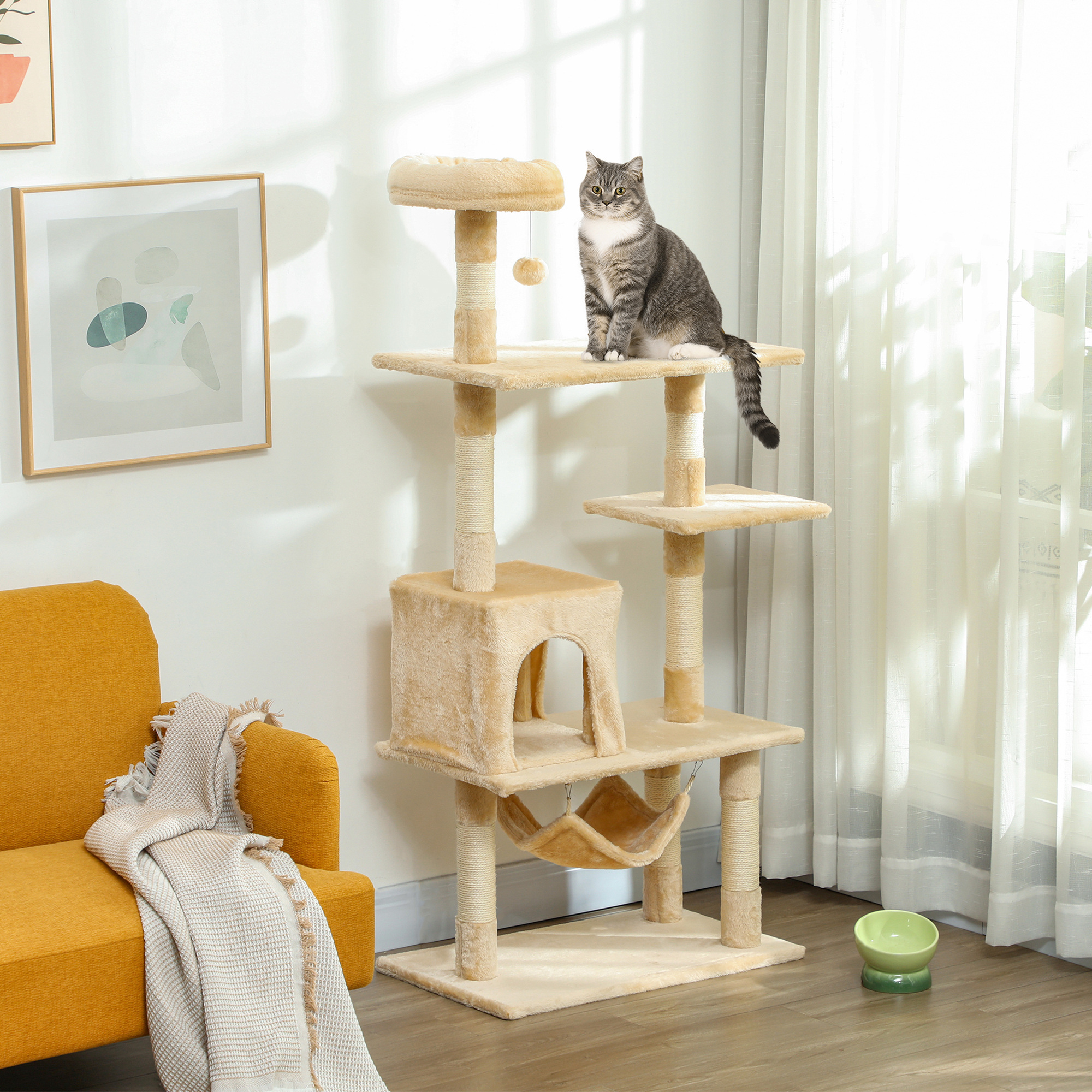 Un gato está sentado en un árbol para gatos multinivel con una hamaca, juguetes y un cuenco en una habitación.