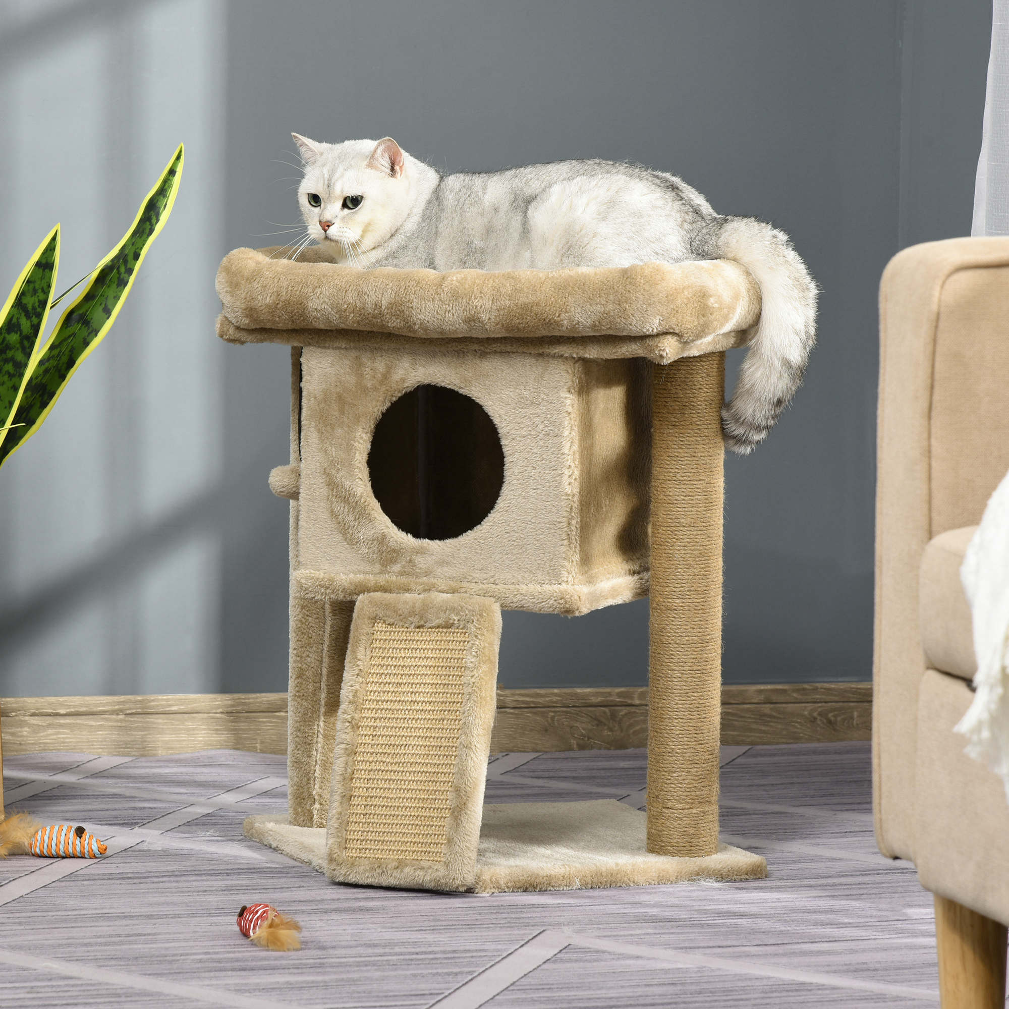 Un árbol para gatos con un gato encima y ratones de juguete en el suelo junto a un sofá.