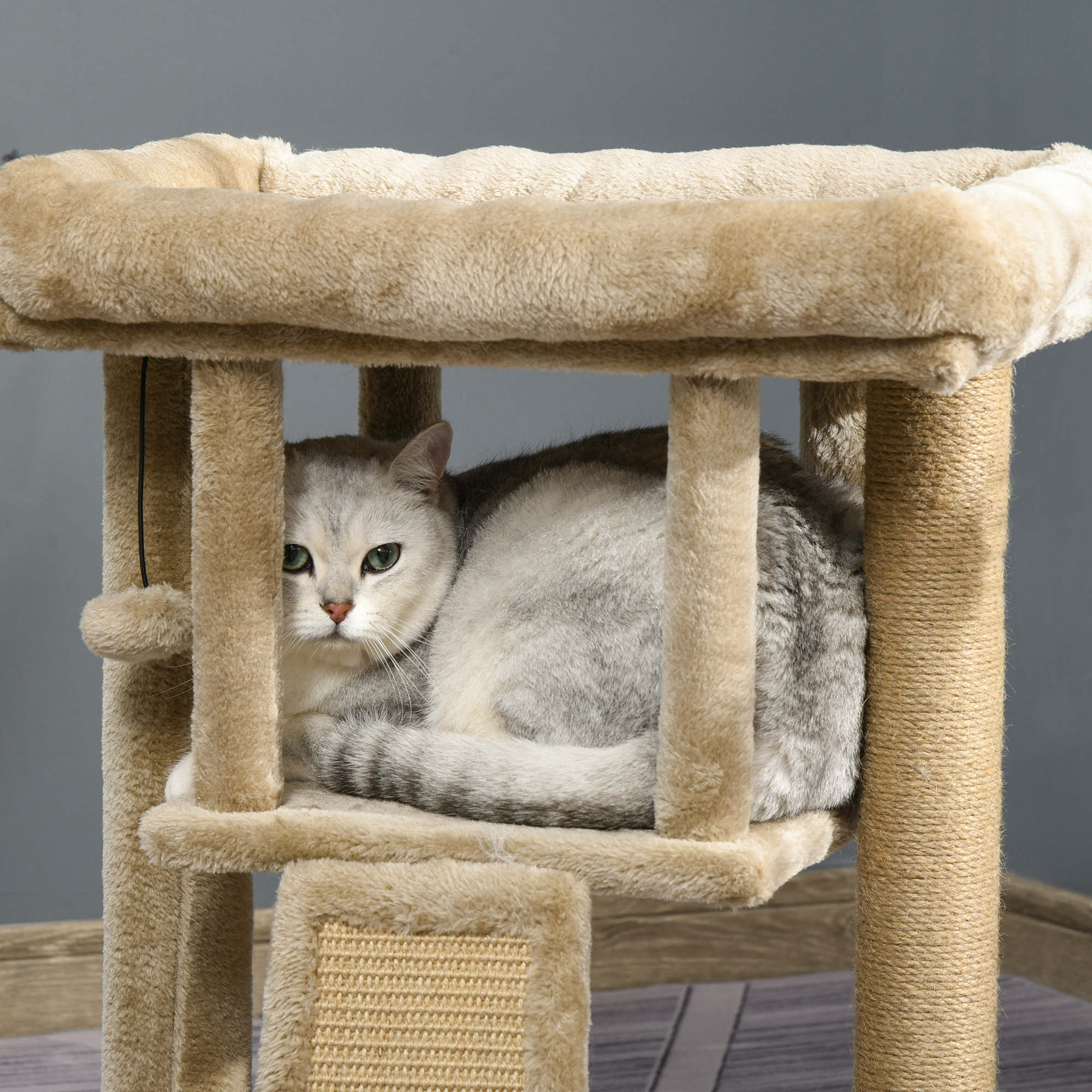 Un gato gris descansa dentro de un árbol para gatos beige, mirando a la cámara.