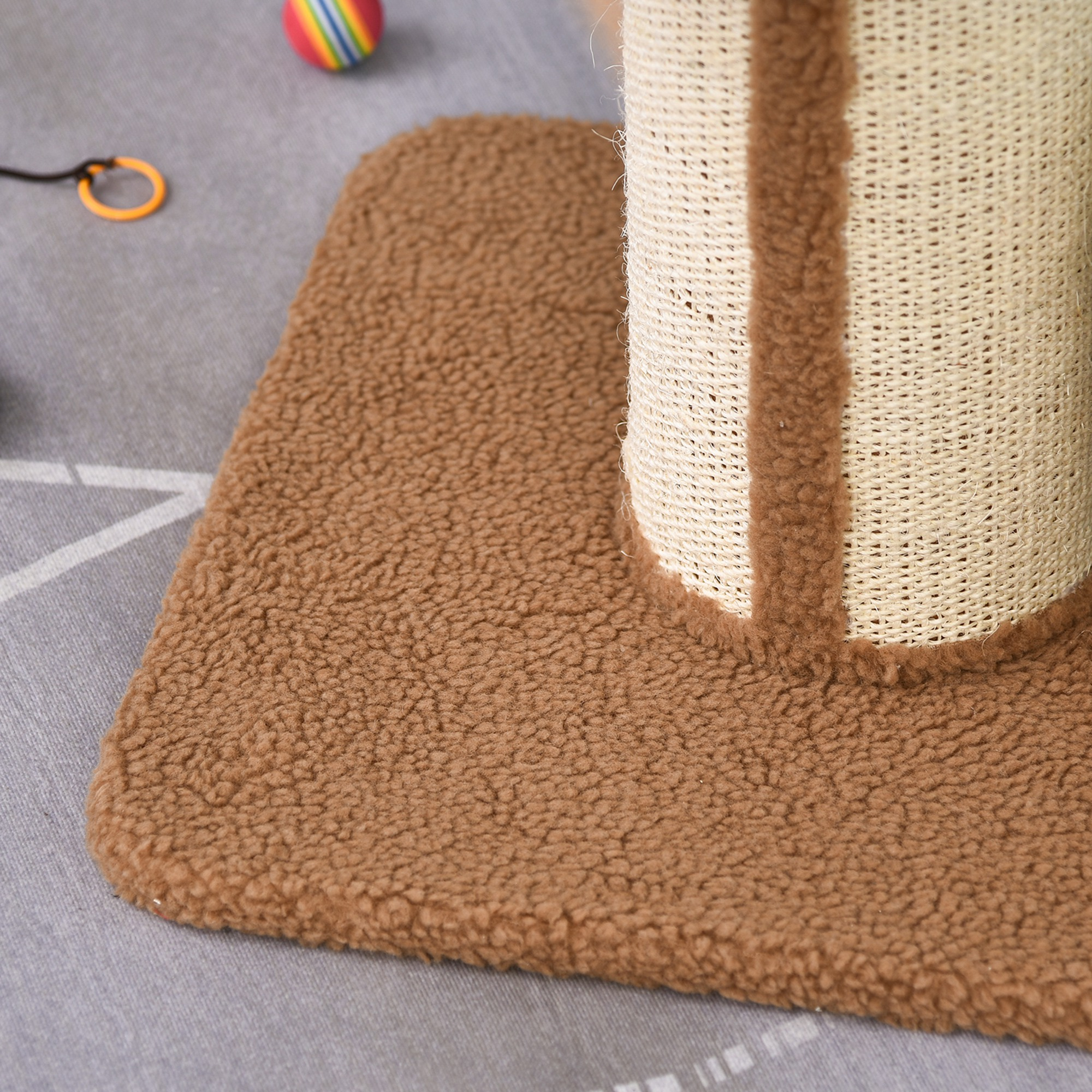 Una alfombra marrón con un rascador para gatos y juguetes. Fondo gris con dos juguetes.