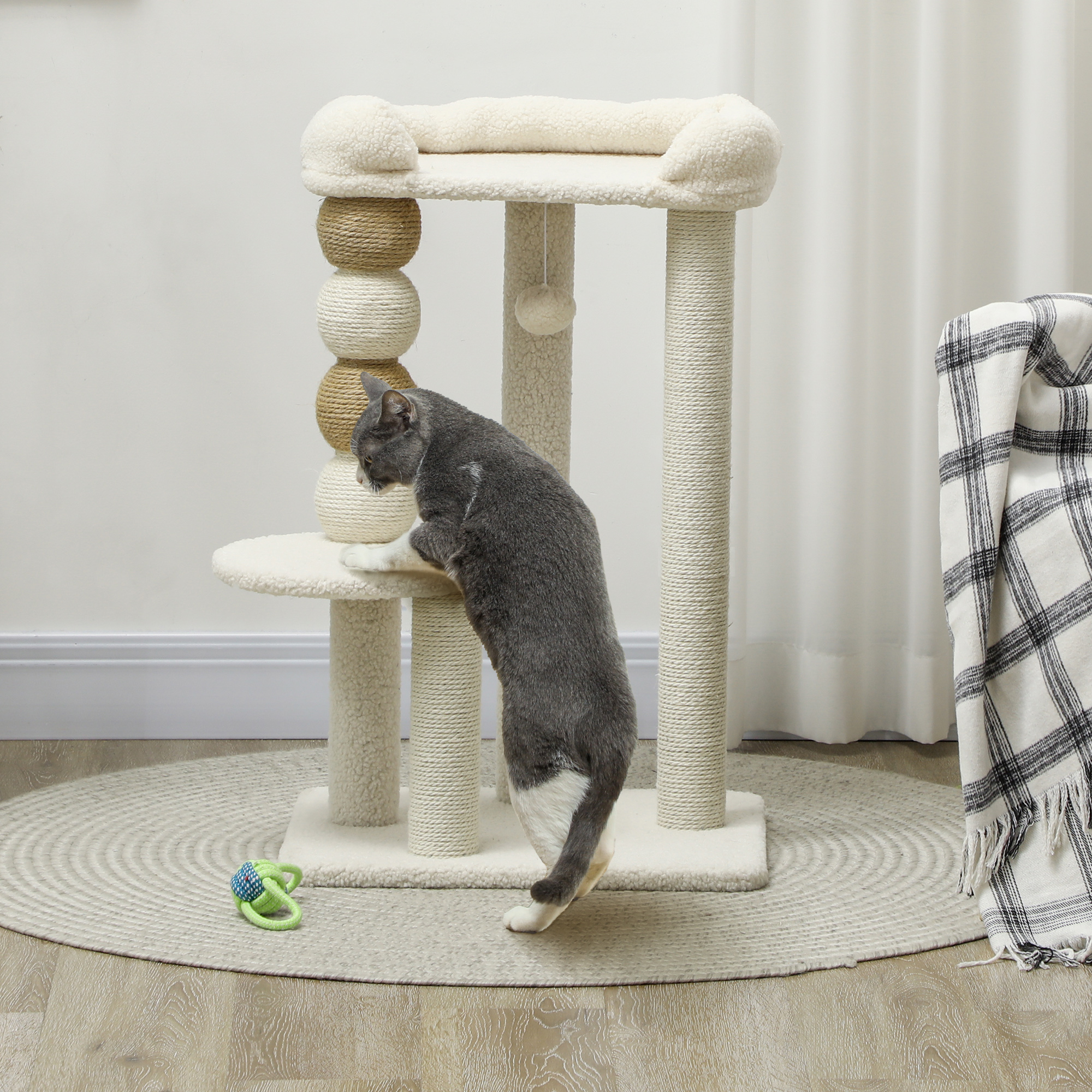 Un gato trepando a un árbol para gatos. El árbol es beige y blanco. Hay una alfombra debajo.