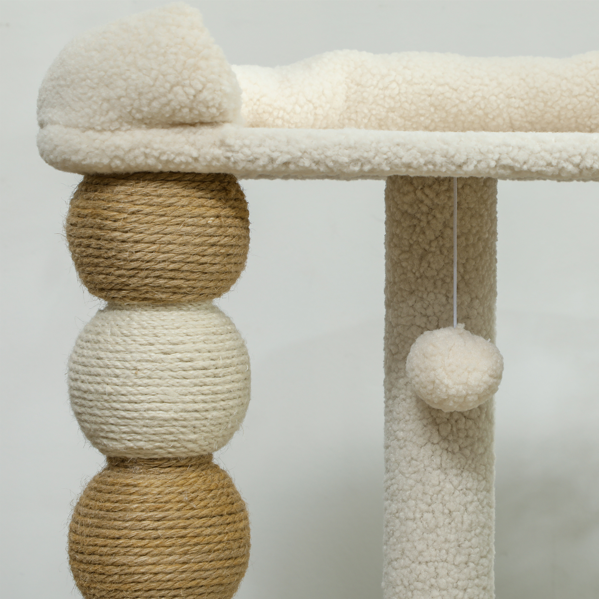 Primer plano de un árbol para gatos con detalles de esferas y cuerdas. Color crema con una bola colgante.