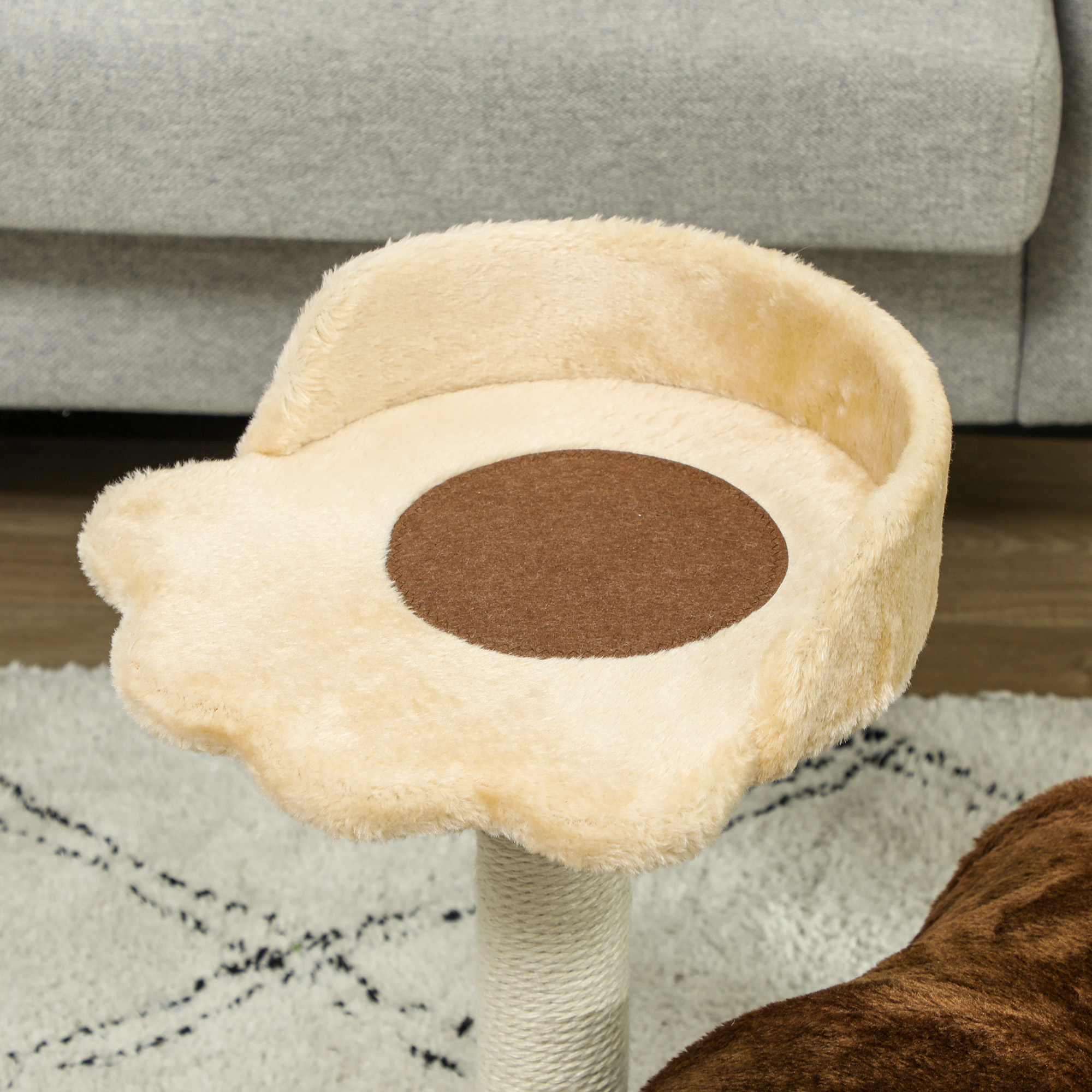 Árbol para gatos con parte superior de felpa beige, centro marrón, poste blanco, sobre alfombra estampada, sofá gris.