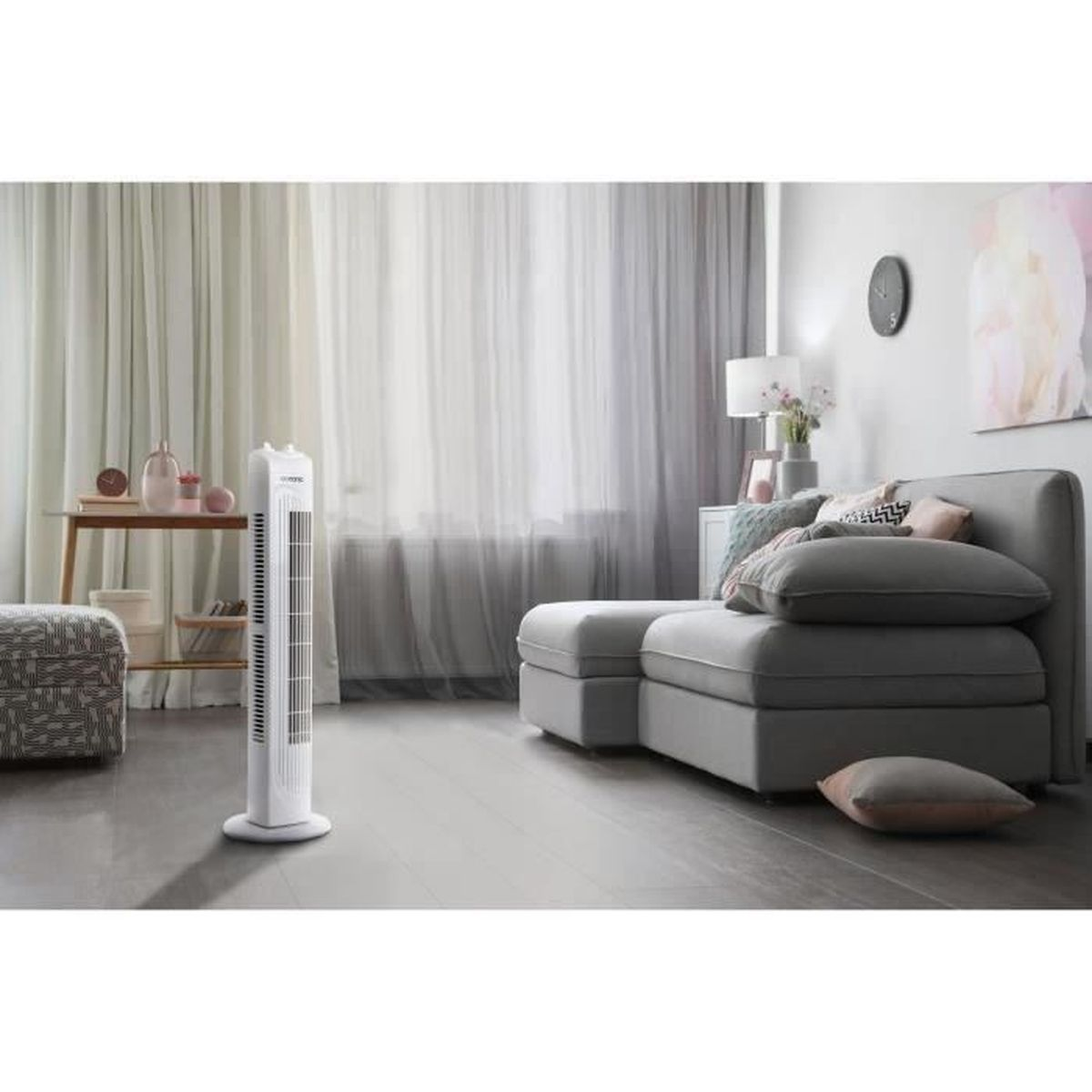 Un ventilatore bianco alto in una stanza. C'è un divano grigio, un tavolo con vasi e un dipinto.