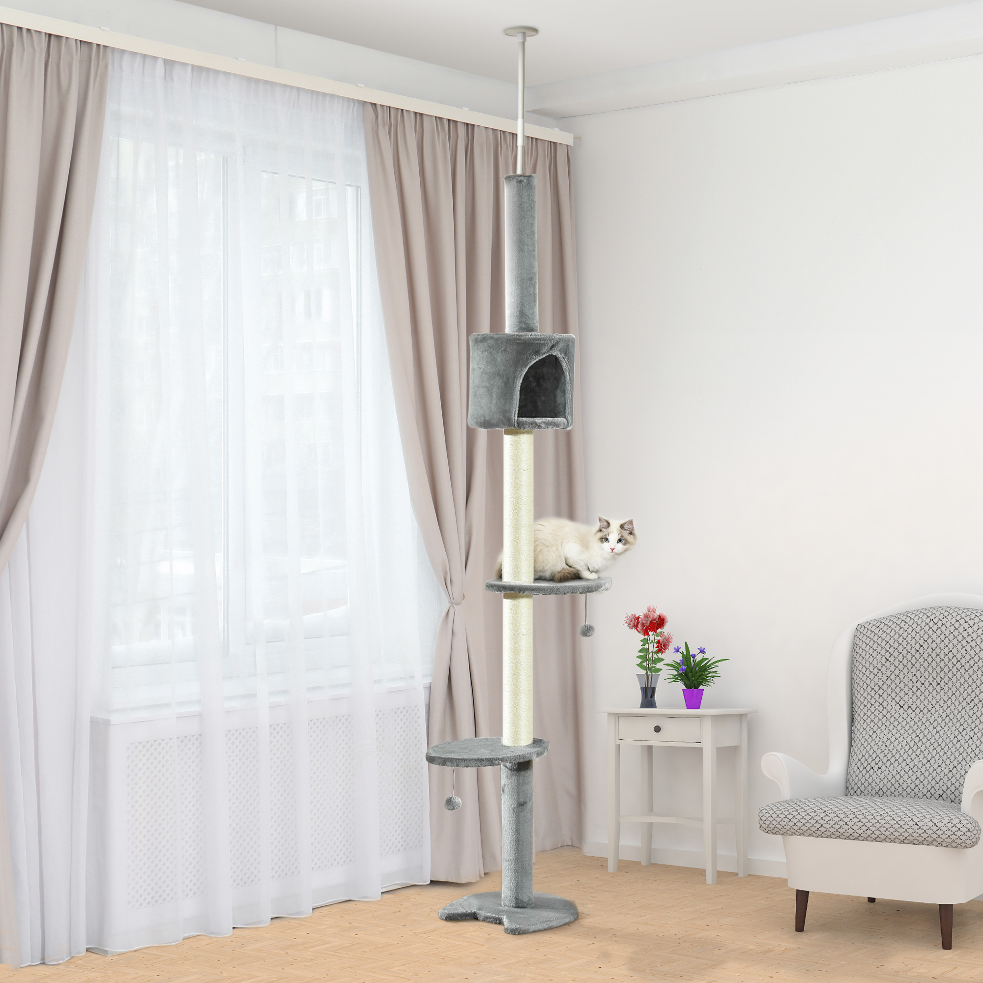 Un gato sentado en un árbol para gatos en una habitación con cortinas, ventana y mesa auxiliar.