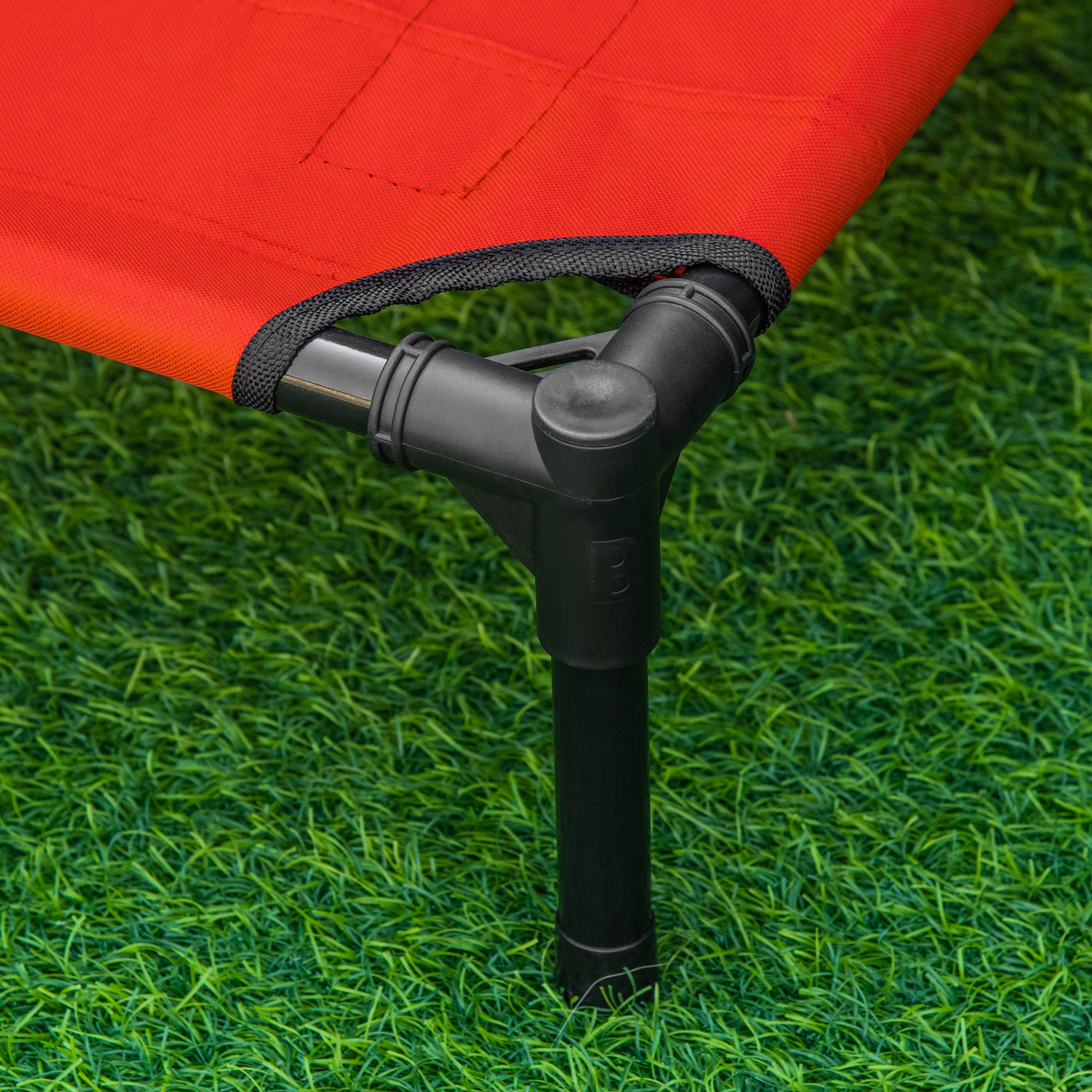 Cama roja para mascotas sobre césped verde. Marco y patas negras. Para que perros y gatos descansen.