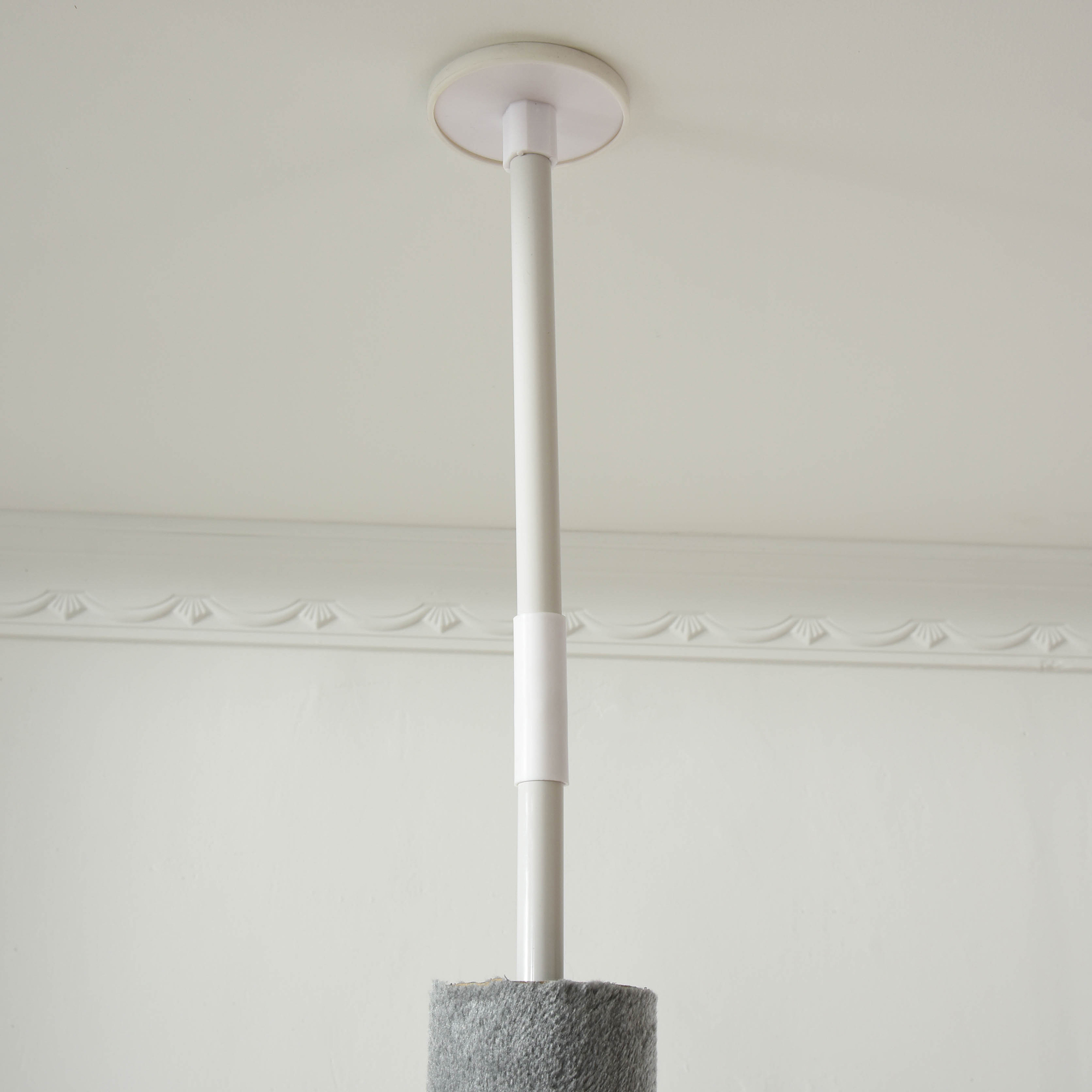 Poste de árbol para gatos blanco montado en el techo con base de poste rascador gris, techo blanco.