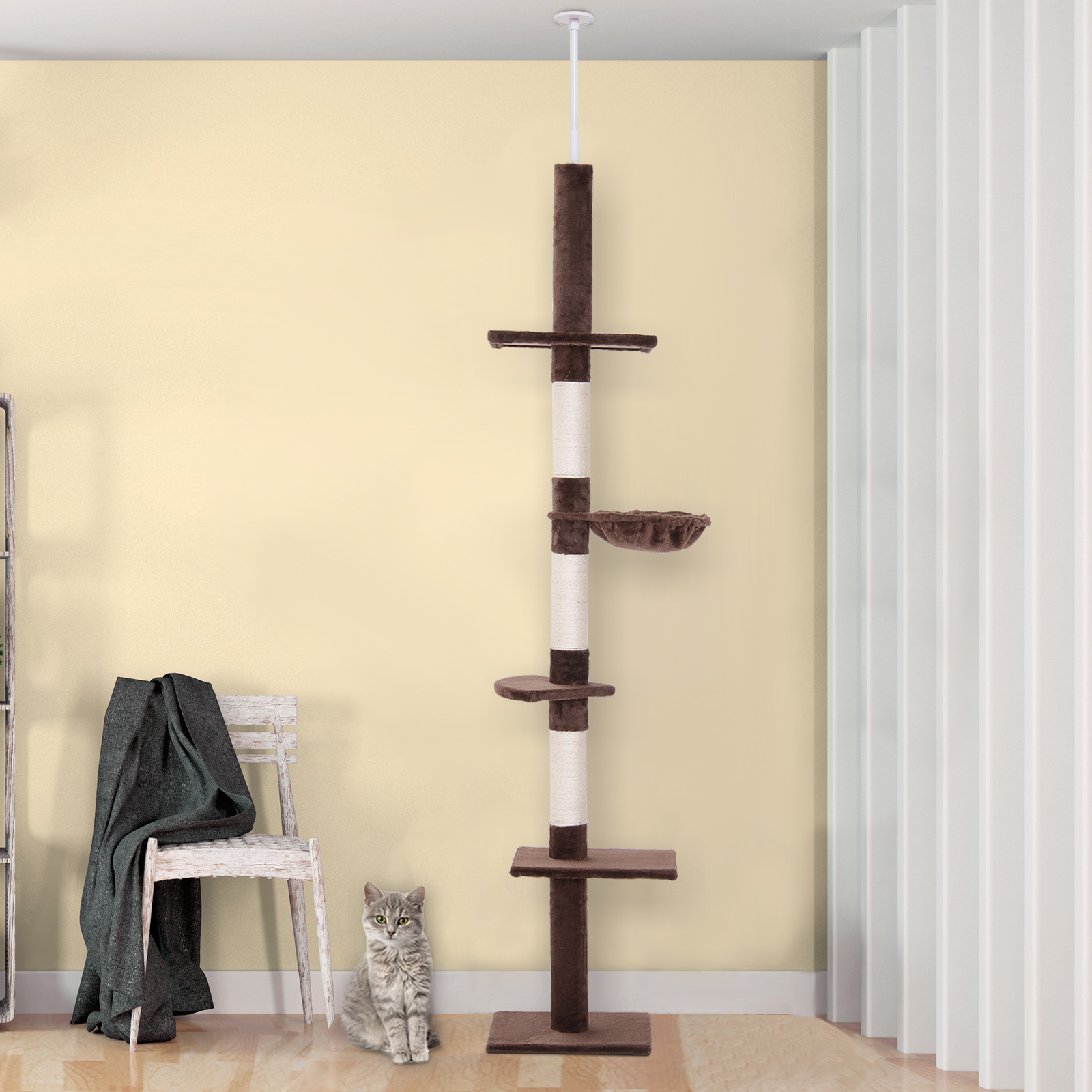 Árbol para gatos con un gato. El árbol está en una pared amarillo claro. El gato se sienta junto a una silla.