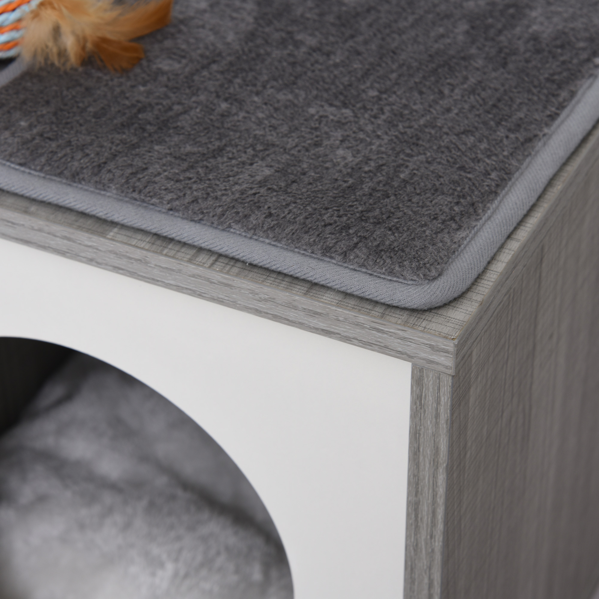 Una casa para gatos con una estera gris encima. La casa es blanca y gris, con una abertura redondeada.