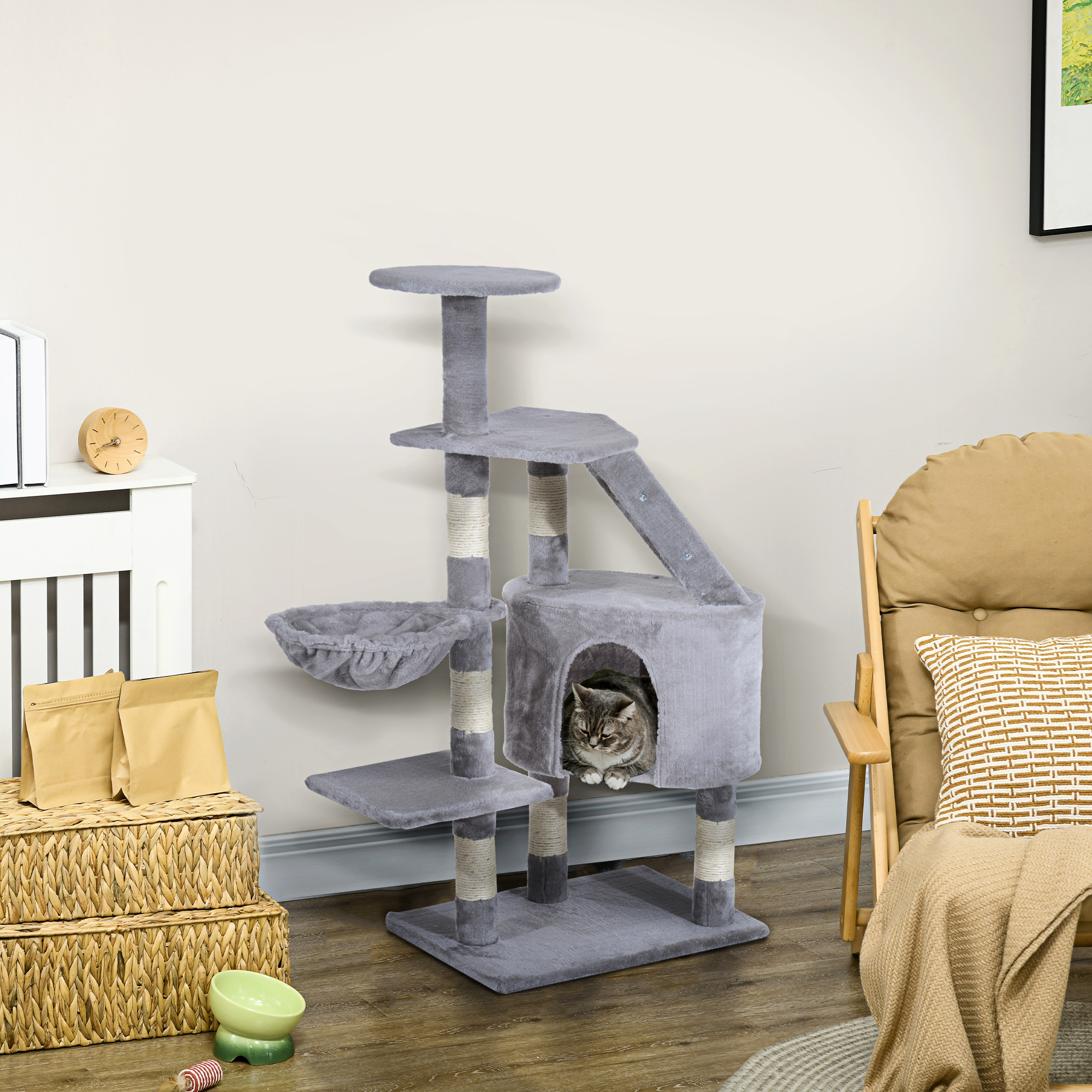 Un árbol para gatos gris de varios niveles con un gato sentado dentro de una cama.