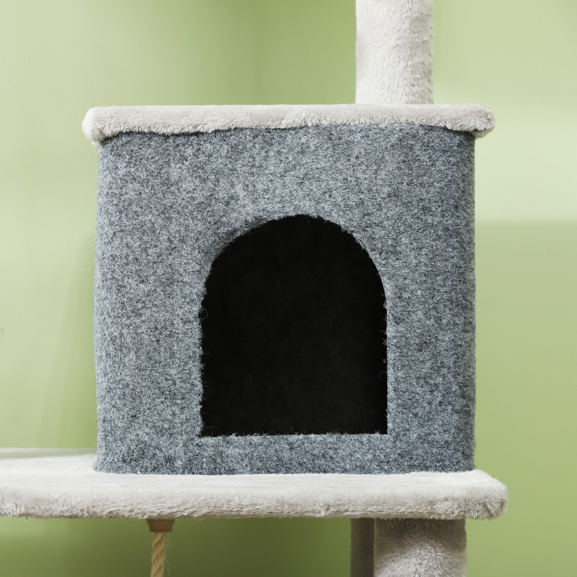 Casa para gatos gris con techo redondo y entrada circular sobre fondo verde.