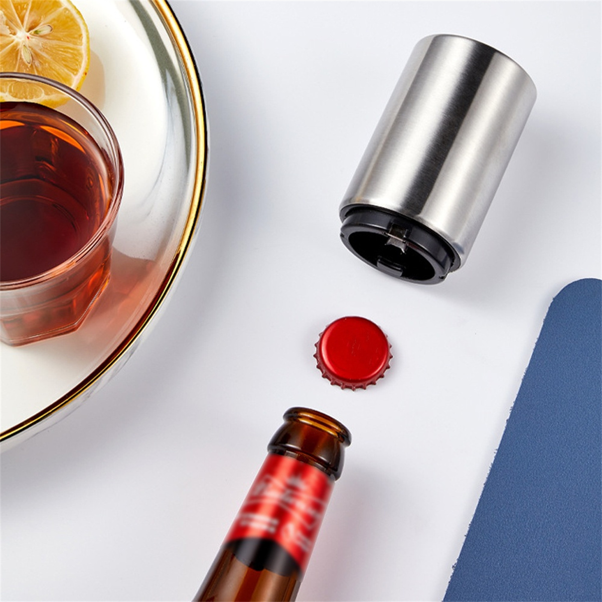 Flaschenöffner, roter Verschluss und ein halb gefülltes Glas dunkler Flüssigkeit. Weißer Hintergrund.