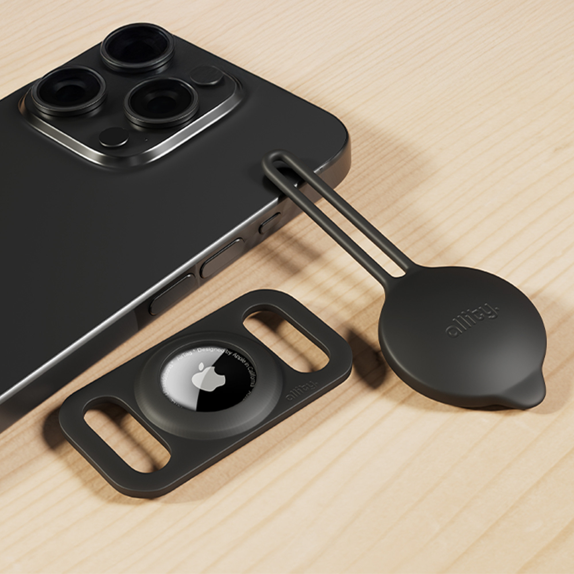 Czarny telefon, AirTag i silikonowy uchwyt na drewnianej powierzchni.
