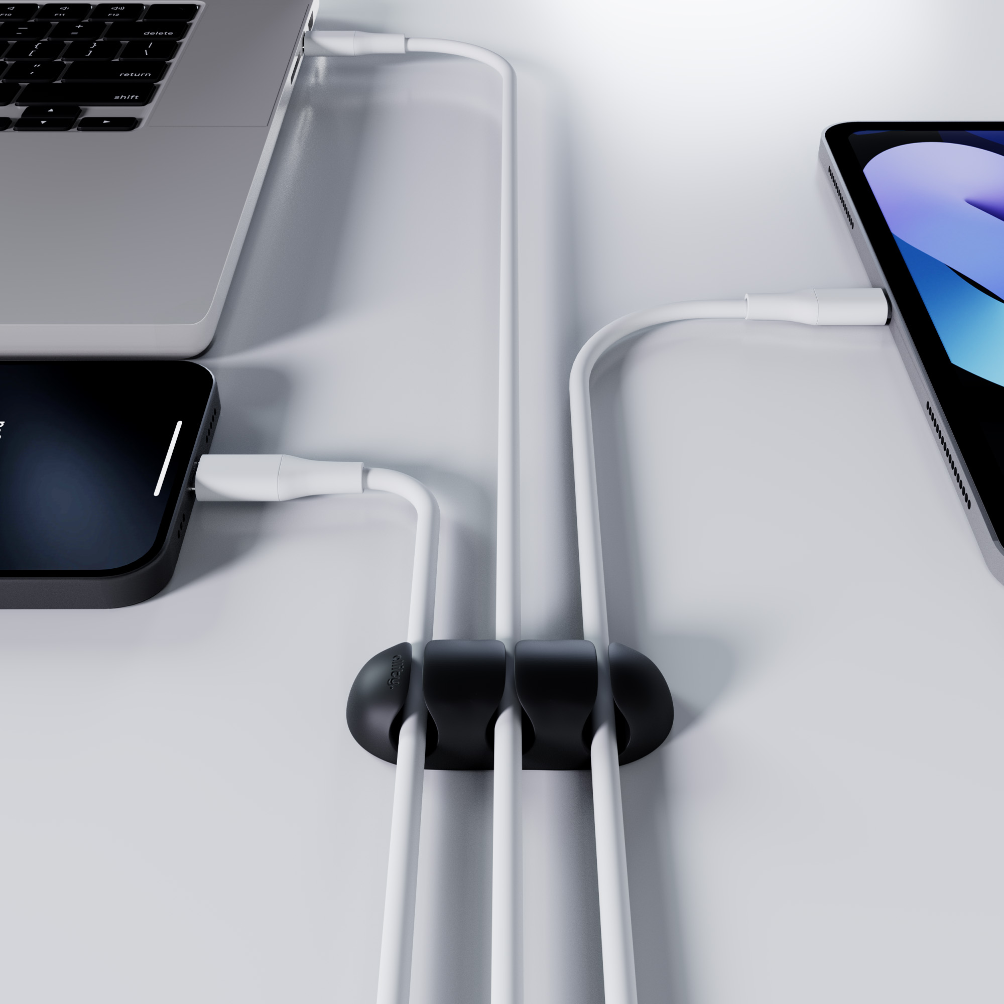Białe kable podłączone do laptopa, telefonu i tabletu z czarnym organizerem kabli.