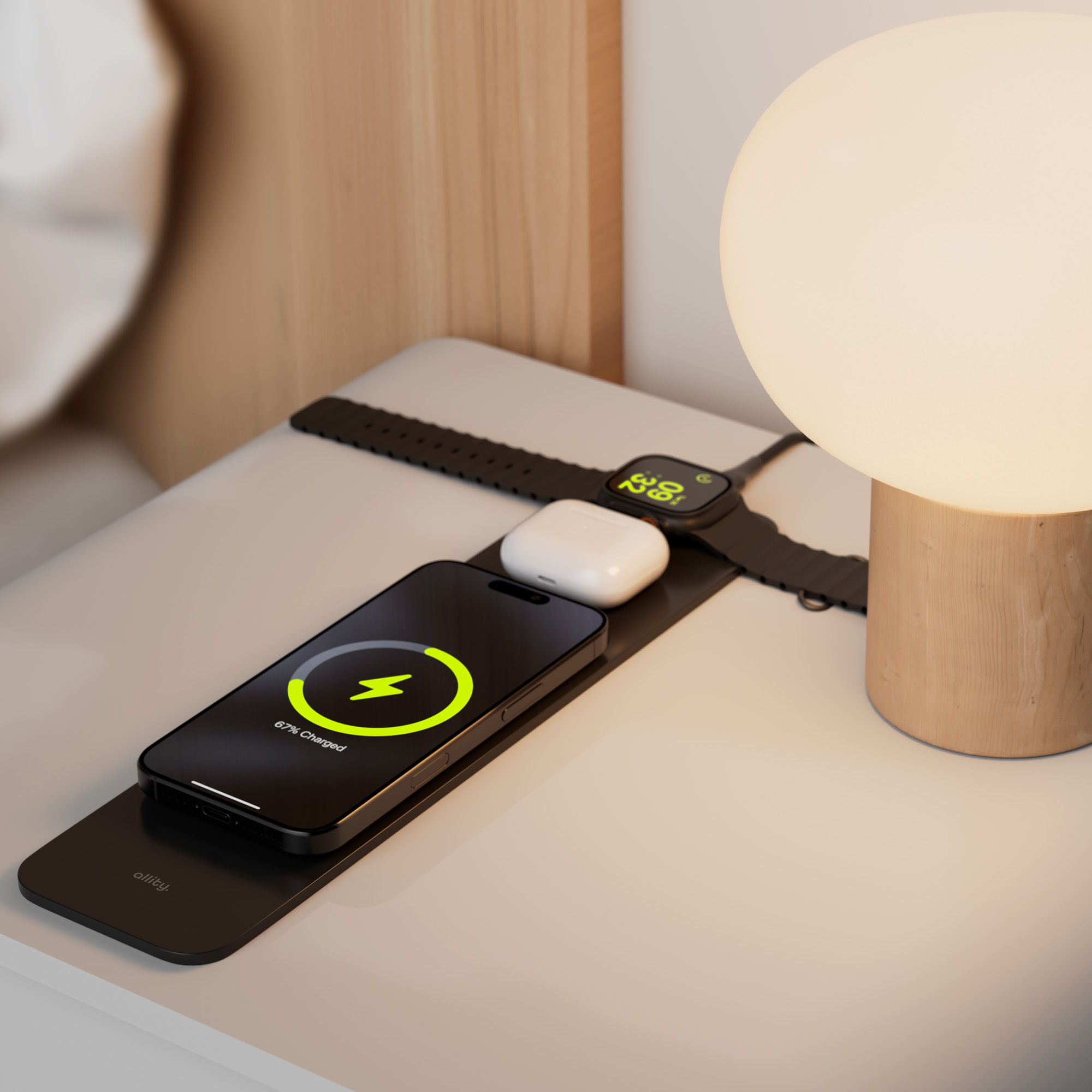 Telefon na podkładce ładującej, w trakcie ładowania. Lampa i zegarek na szafce nocnej.