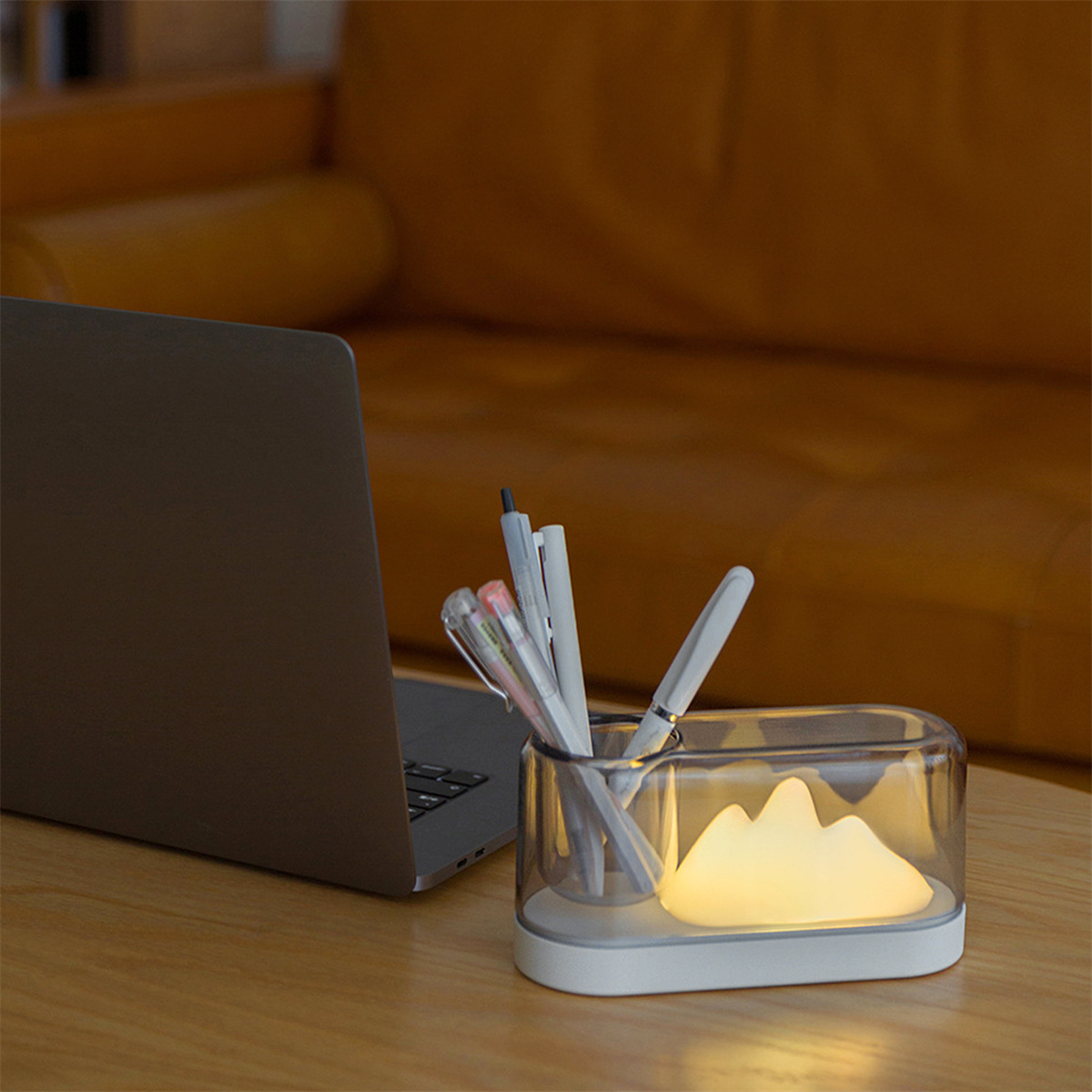 Ein Tisch mit einem Laptop und einem transparenten Stifthalter mit Stiften und einem beleuchteten Berg.