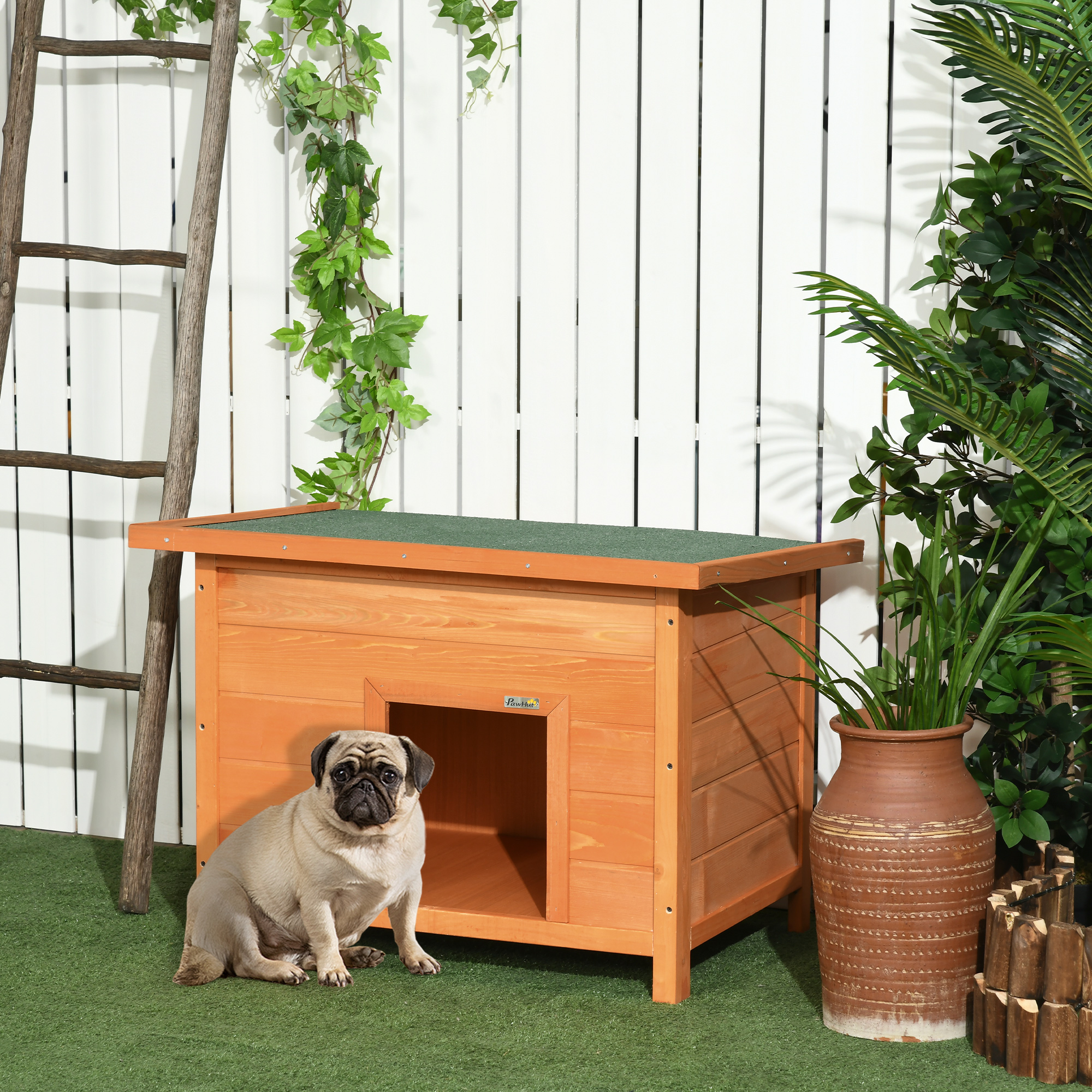 Una caseta de perro de madera con un pug sentado frente a ella. La casa está en un jardín con plantas.