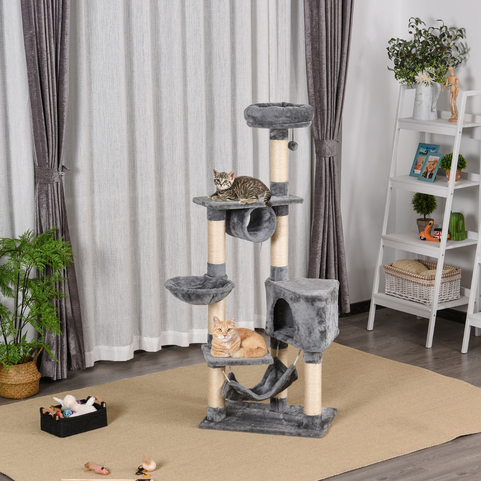 Un árbol para gatos con dos gatos encima. Un gato está en una hamaca. Una planta y una estantería en el fondo.