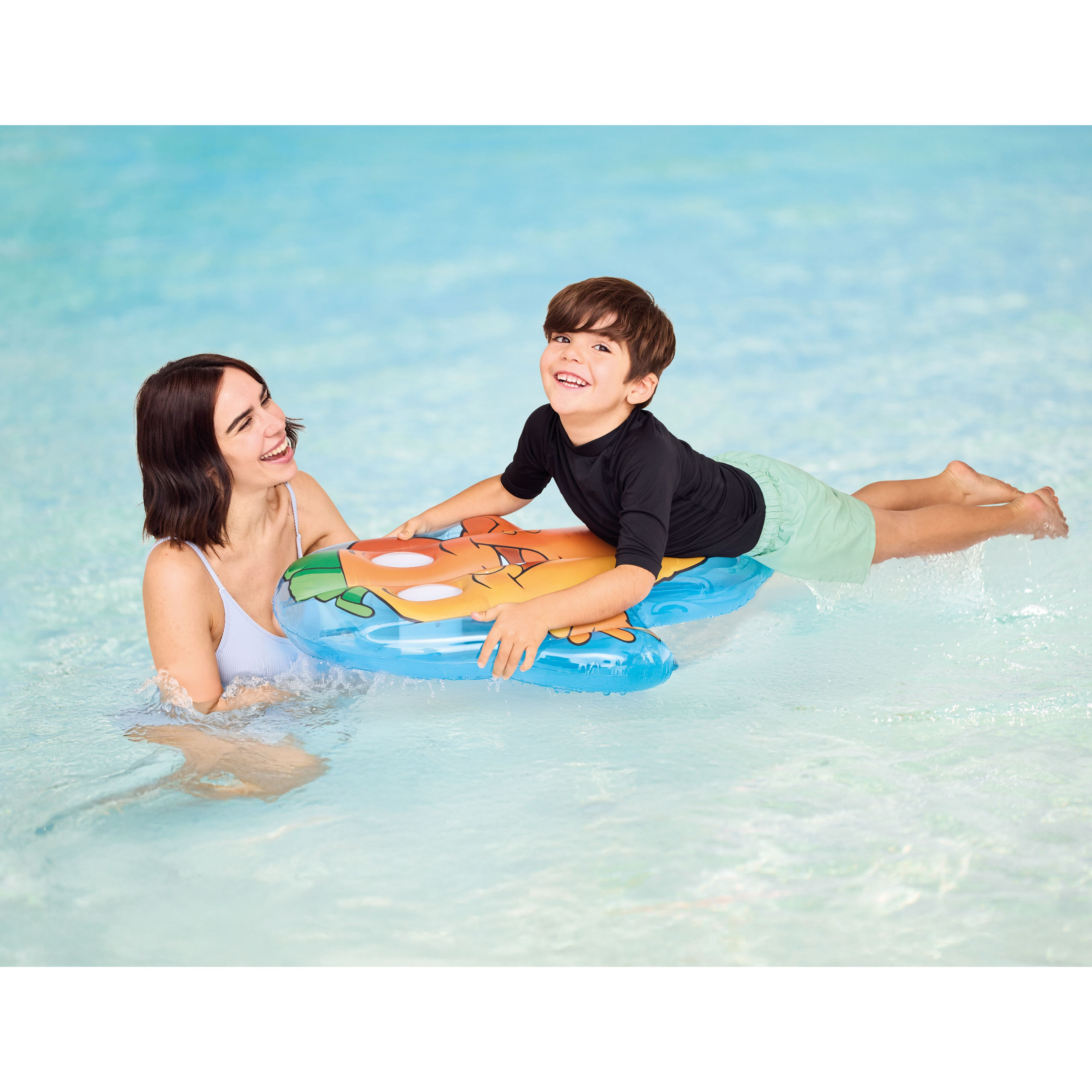Eine Frau und ein Junge sind in einem Pool. Der Junge liegt auf einem Schwimmreifen und lächelt.