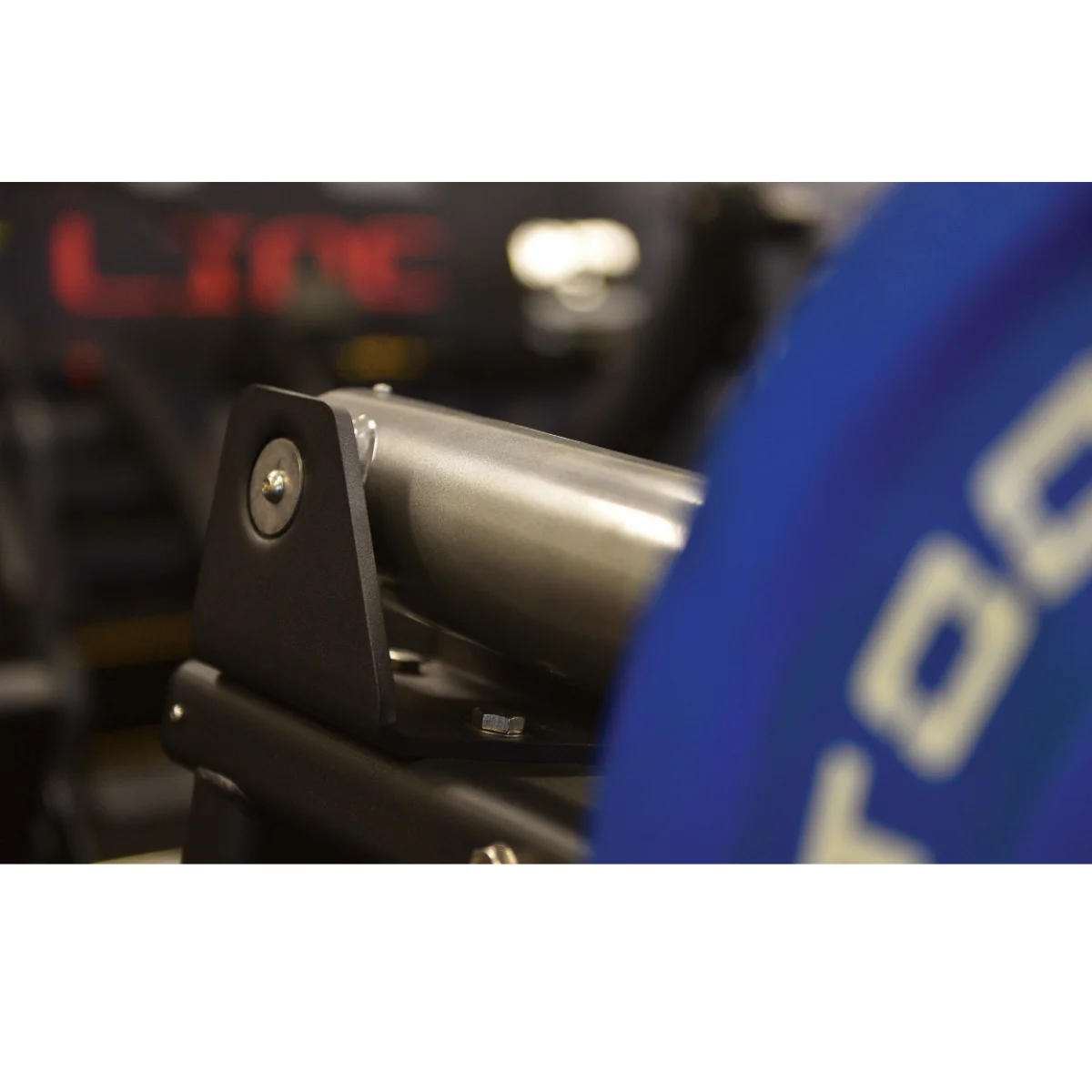 Close-up van een grijs onderdeel van een trainingsmachine, met een blauwe gewichtplaat zichtbaar.