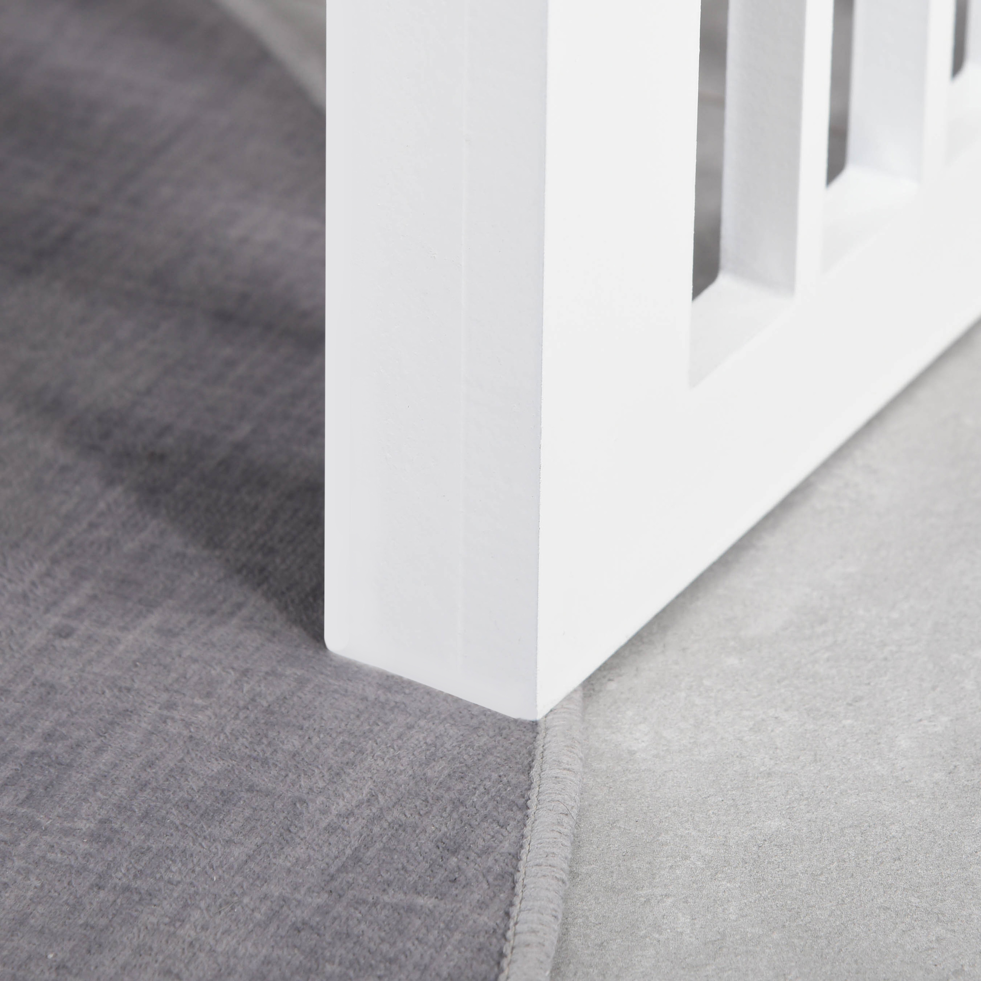 Primer plano de una estructura de madera blanca sobre un piso gris con una alfombra.
